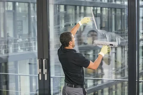 Man cleaning large glass window with squeegee in a modern building.