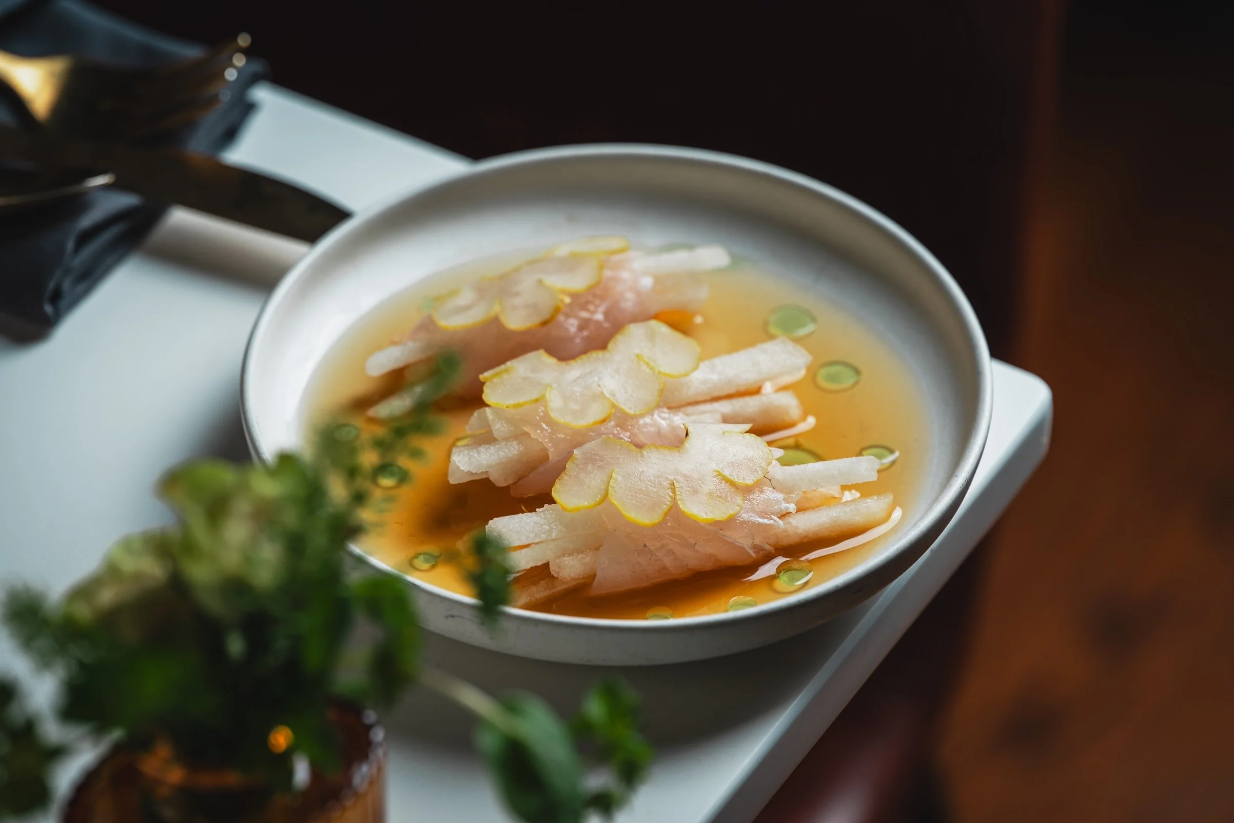 A beautifully plated piece of fish served on a bed of creamy sauce, garnished with fresh greens on a white background.