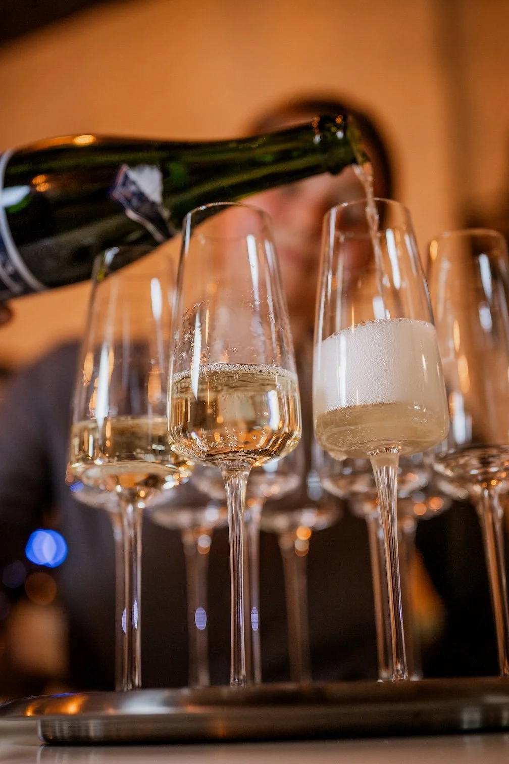 A person pouring champagne into flute glasses for a private dining event.