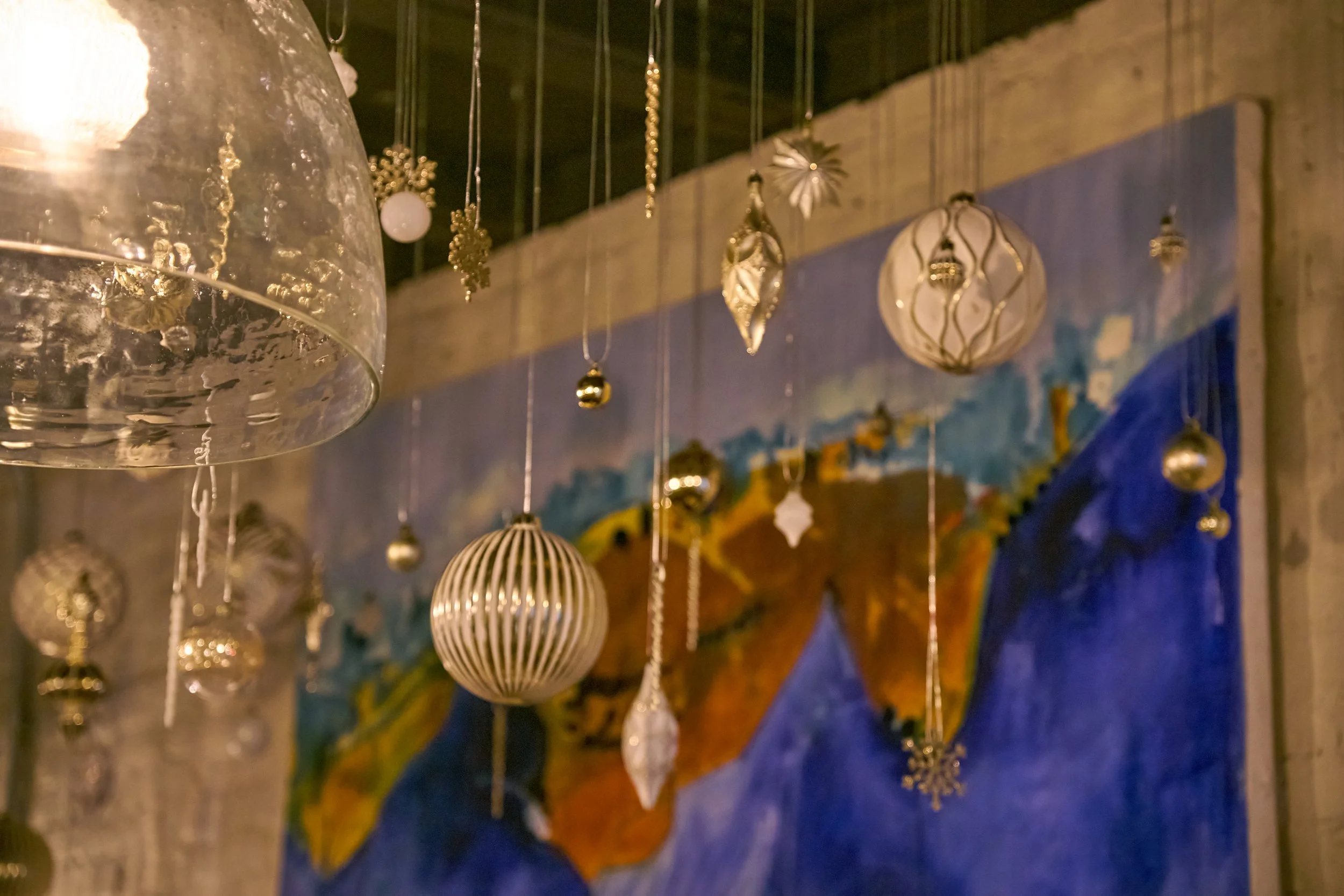 Hanging Christmas ornaments, including various spherical and icicle shapes, in front of a colorful abstract painting.