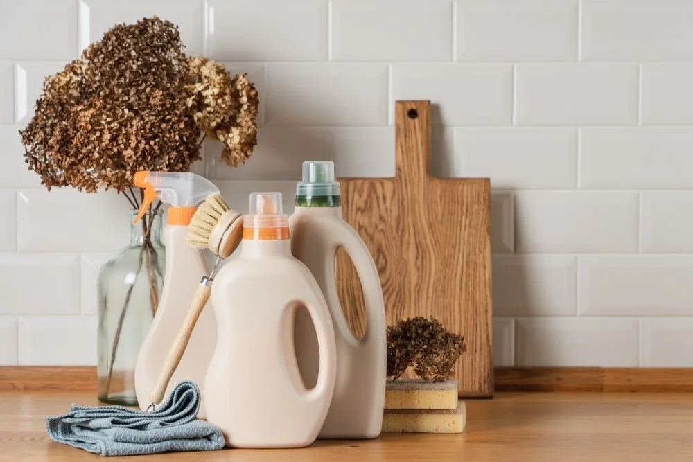 Person pouring cleaning solution into a vintage-style mop bucket with a wringer, containing a wooden mop handle and mop head.