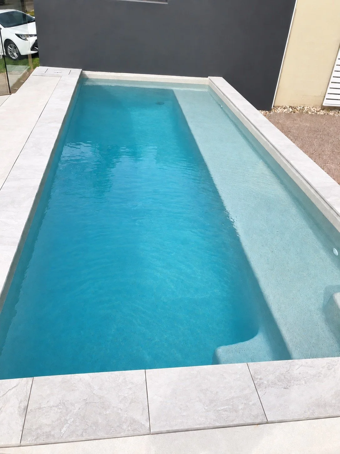 Narrow swimming pool with a long shallow bench and pale stone coping in Sippy Downs.