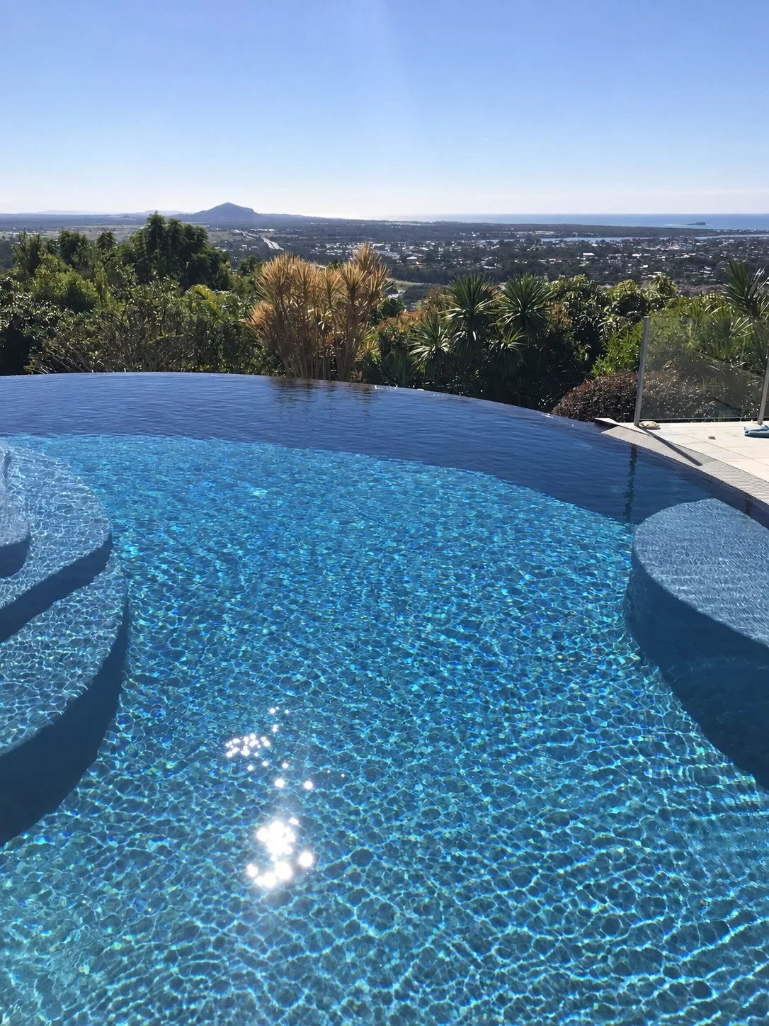 Sunlit infinity pool with curved steps overlooking the Sunshine Coast from Buderim.