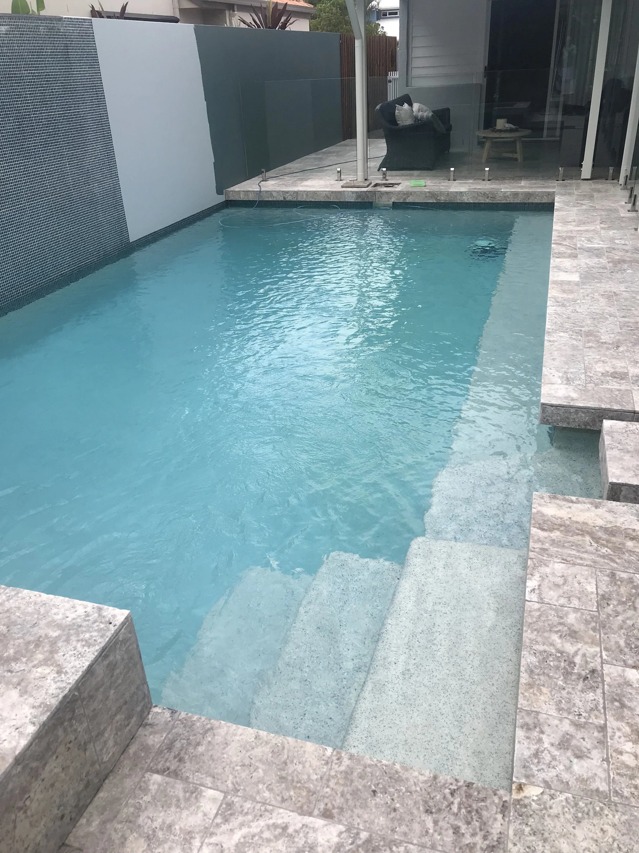 Courtyard swimming pool with broad submerged entry steps, pale stone paving and a tall feature wall in Bokarina.