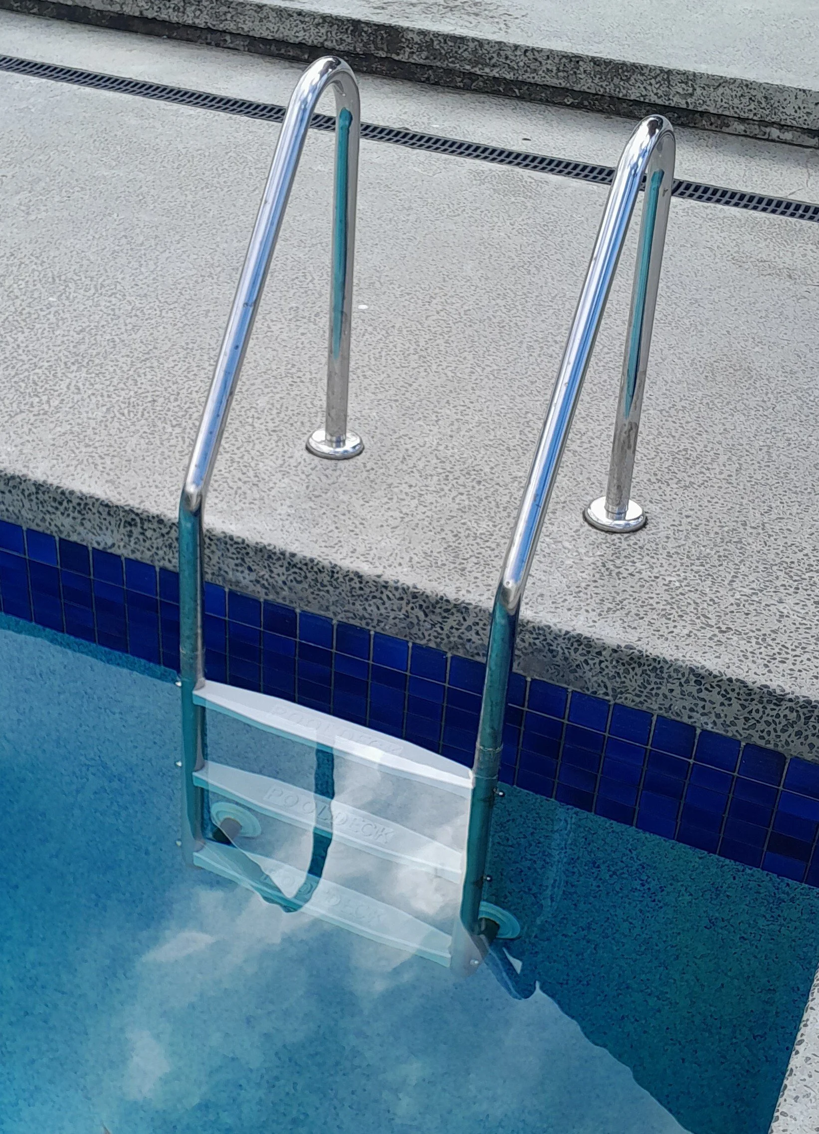 Stainless steel pool ladder rails at the edge of a swimming pool with a blue tile border.