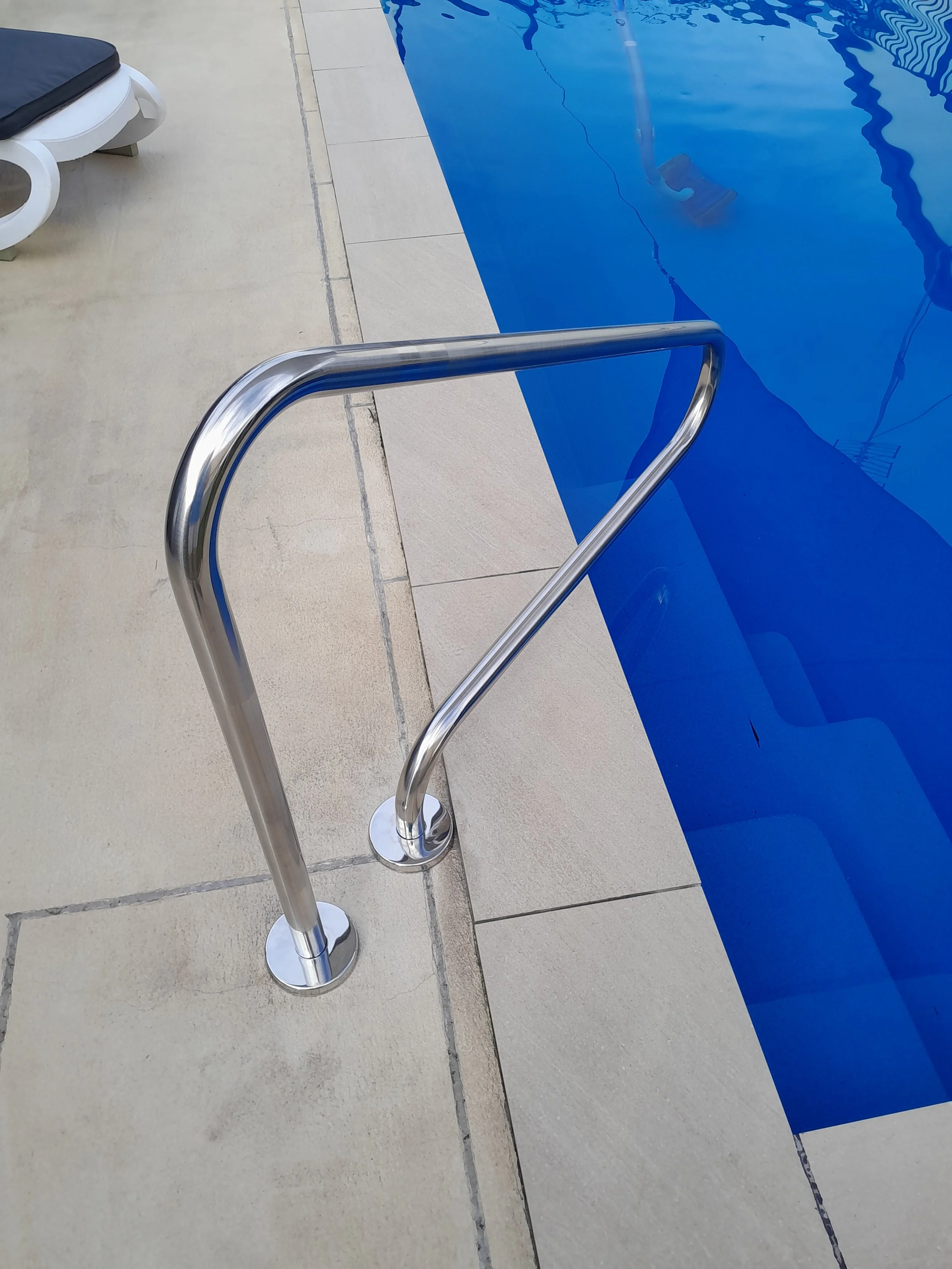 Stainless steel handrail with two round base mounts beside blue swimming pool steps.