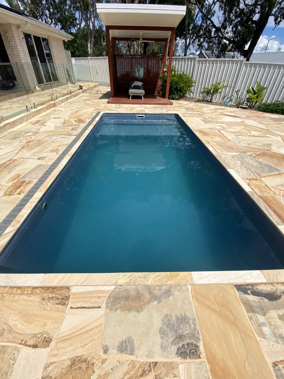 Rectangular pool in Buddina surrounded by natural stone paving, with a timber cabana and lounge chair.