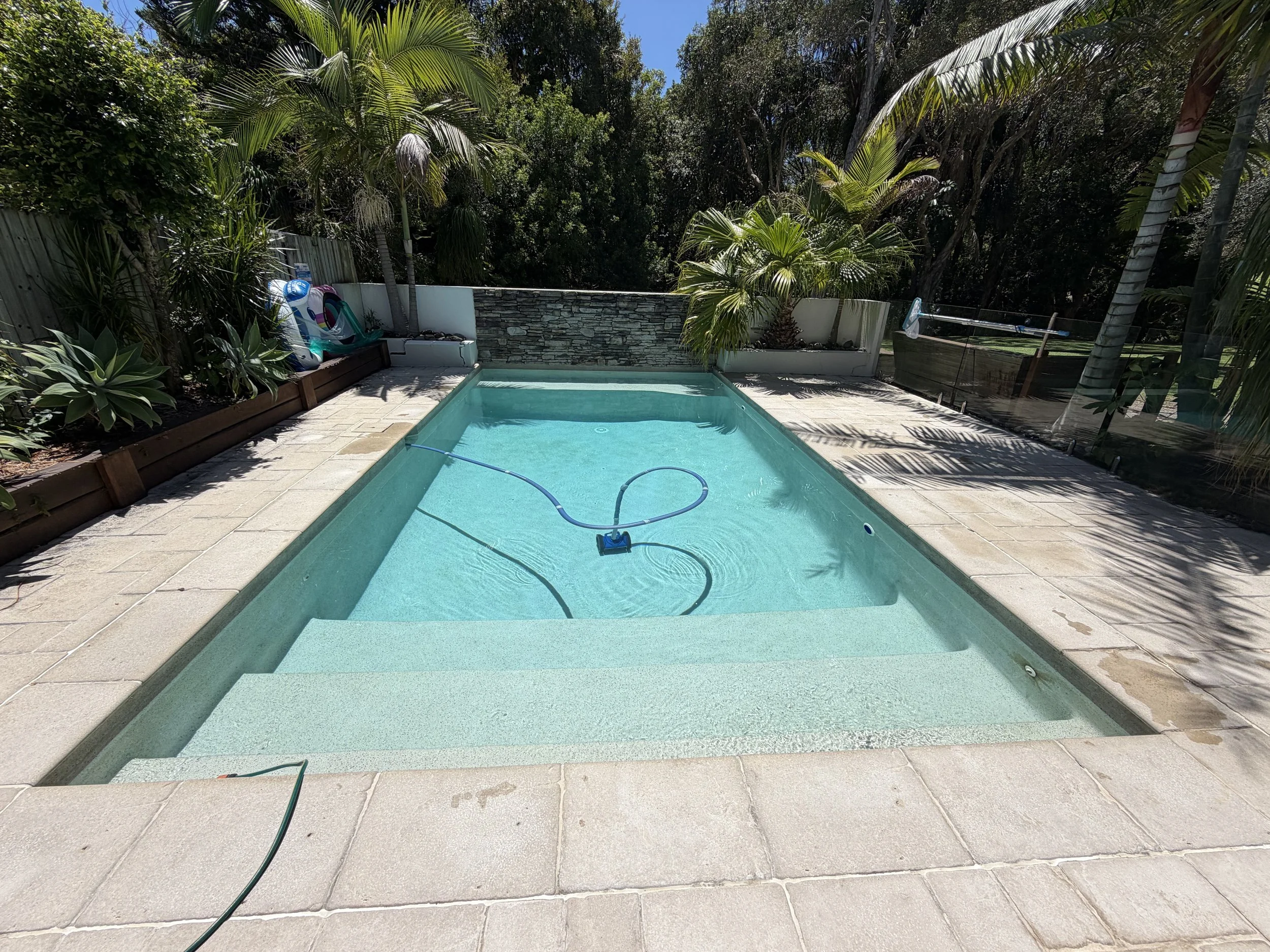 Rectangular backyard pool with a wide shallow entry, a pool cleaner and tropical garden surrounds in Bokarina.
