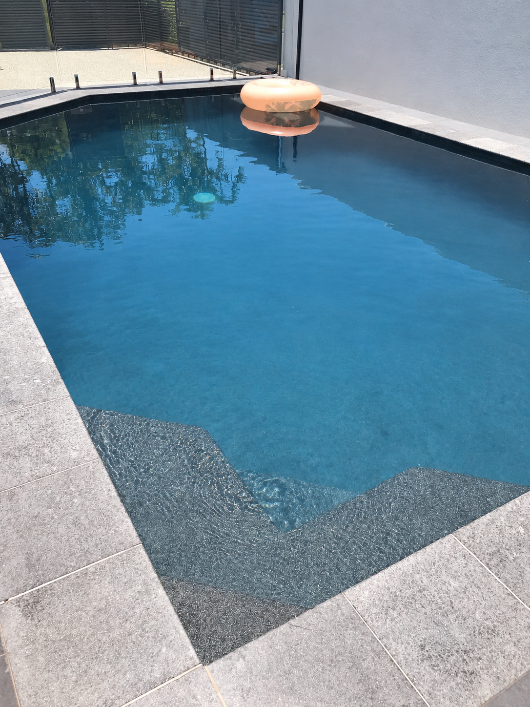 Blue swimming pool with grey tiled coping, submerged steps and an orange pool float in Alexandra Headland.