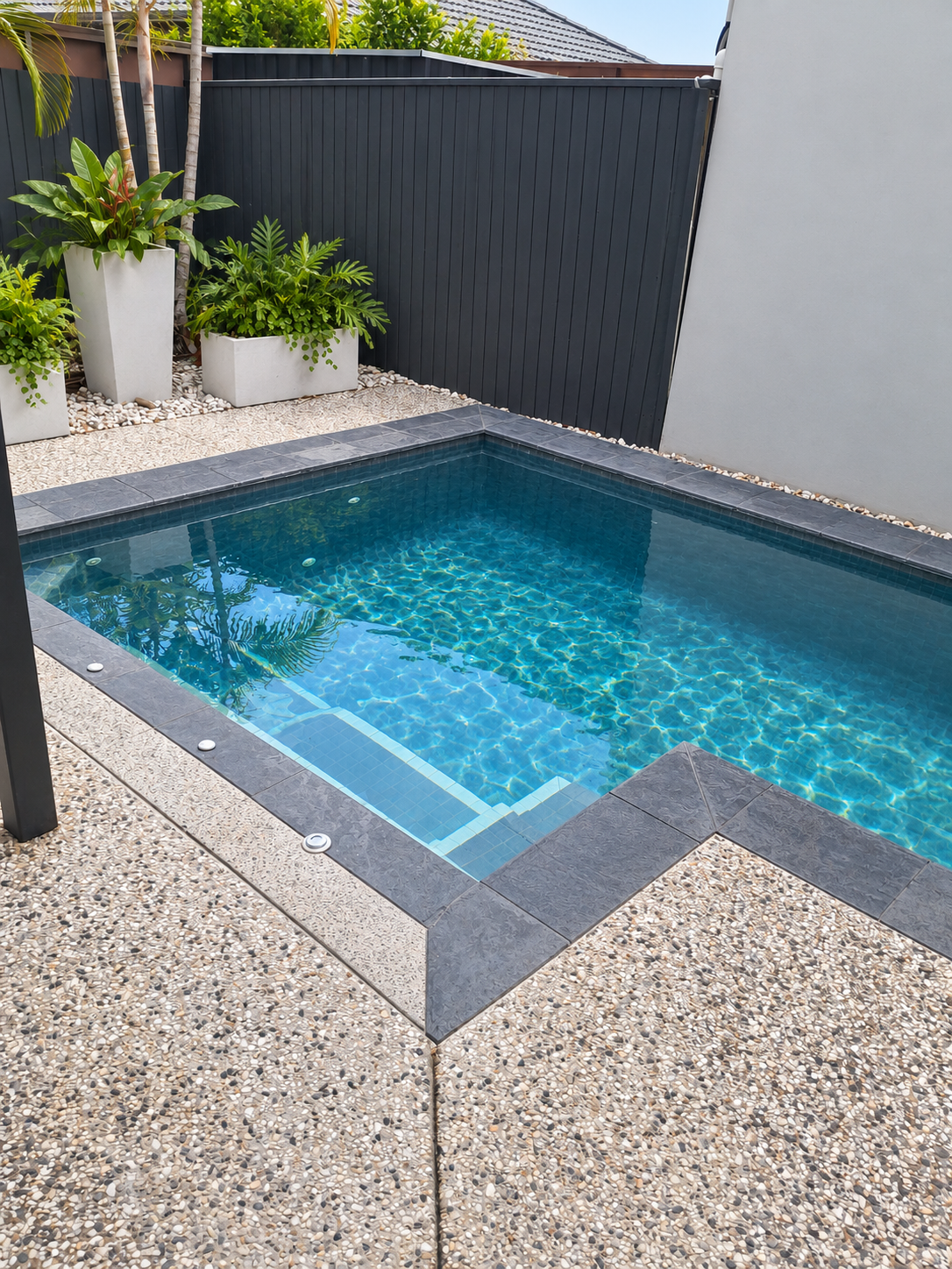 Compact courtyard pool in Kunda Park with blue tiles, dark grey coping and potted tropical plants.