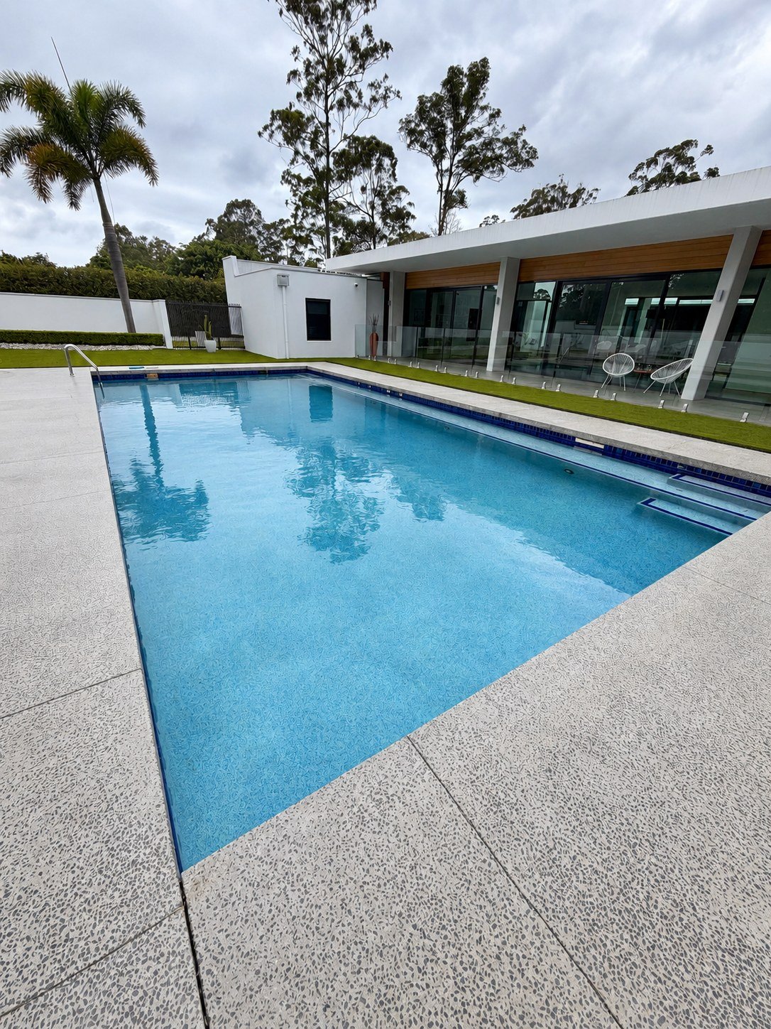 Rectangular swimming pool with textured paving beside a modern home in Tanawha.