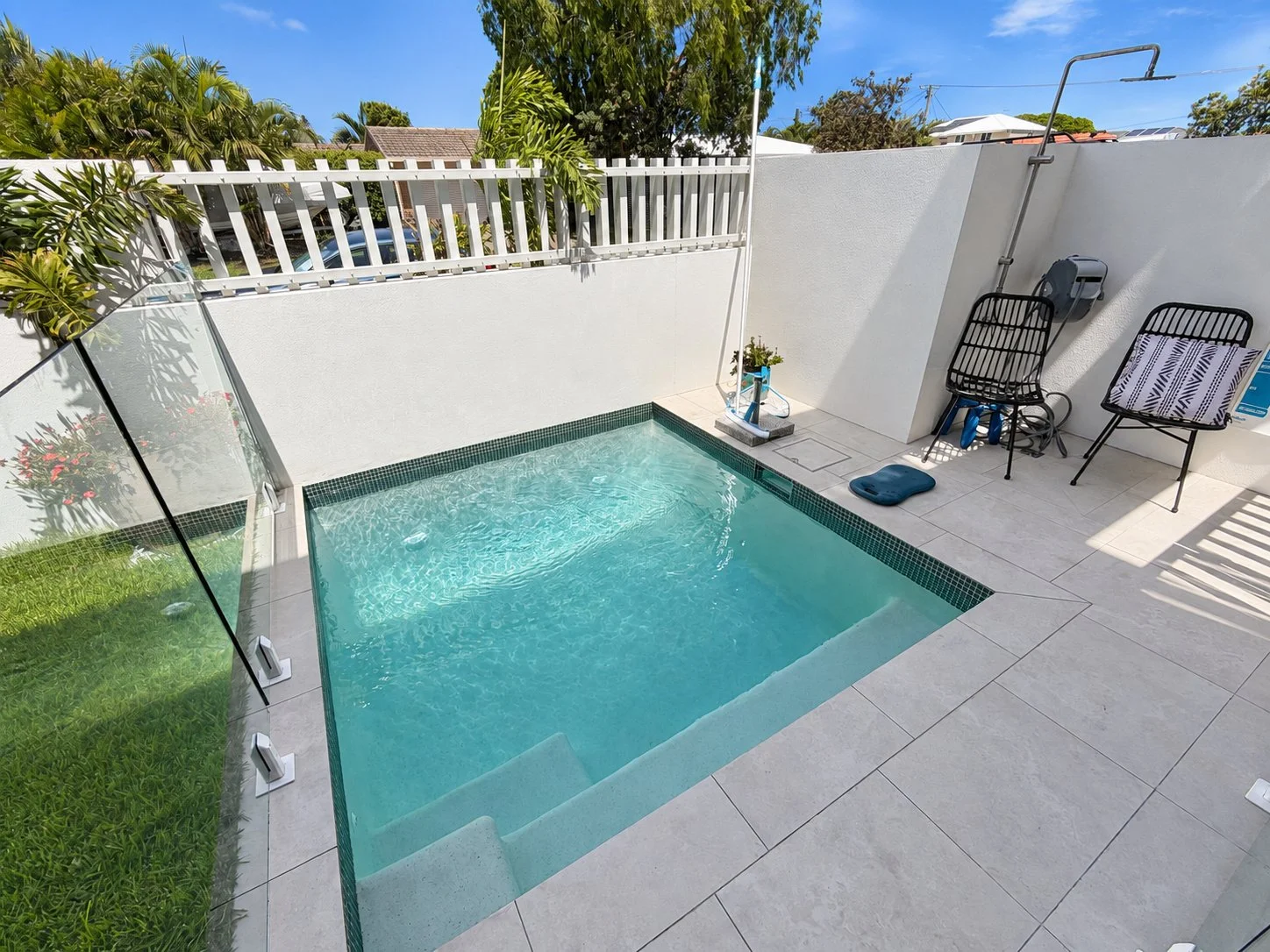 Courtyard plunge pool in Buddina with entry steps, glass fencing, pale paving, two chairs and an outdoor shower.