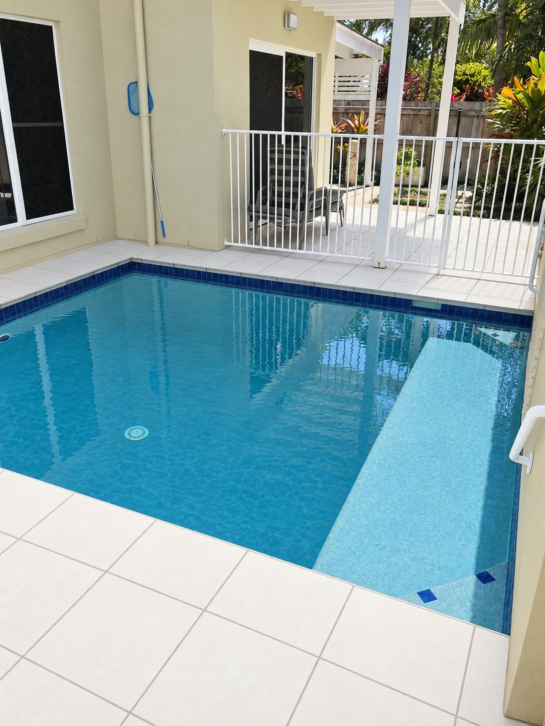 Courtyard swimming pool with clear blue water, a wide submerged ledge, pale tiled surrounds and white pool fencing in Parrearra.