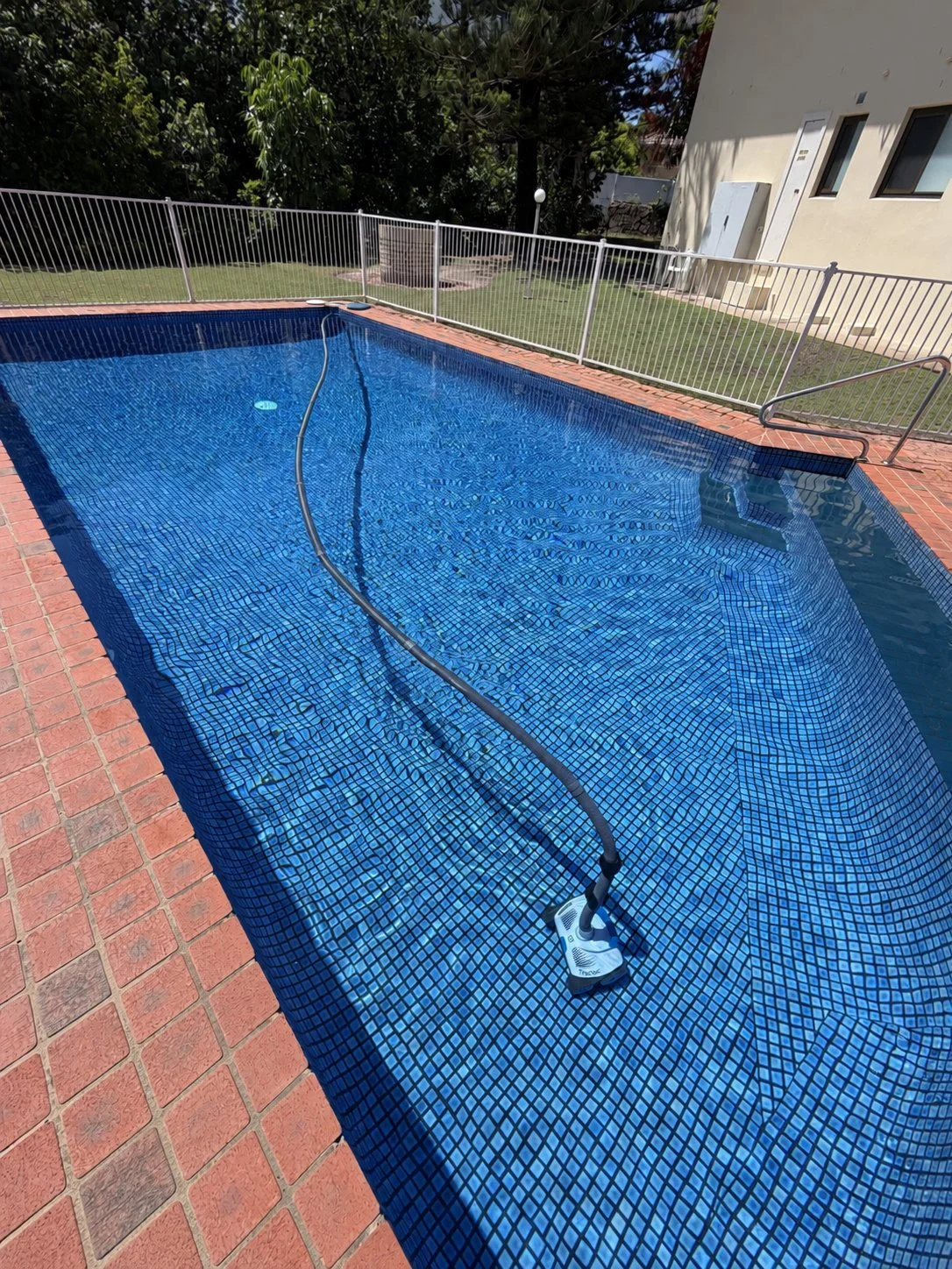 Blue mosaic swimming pool in Buddina with brick coping, an automatic cleaner, entry handrail and safety fence.