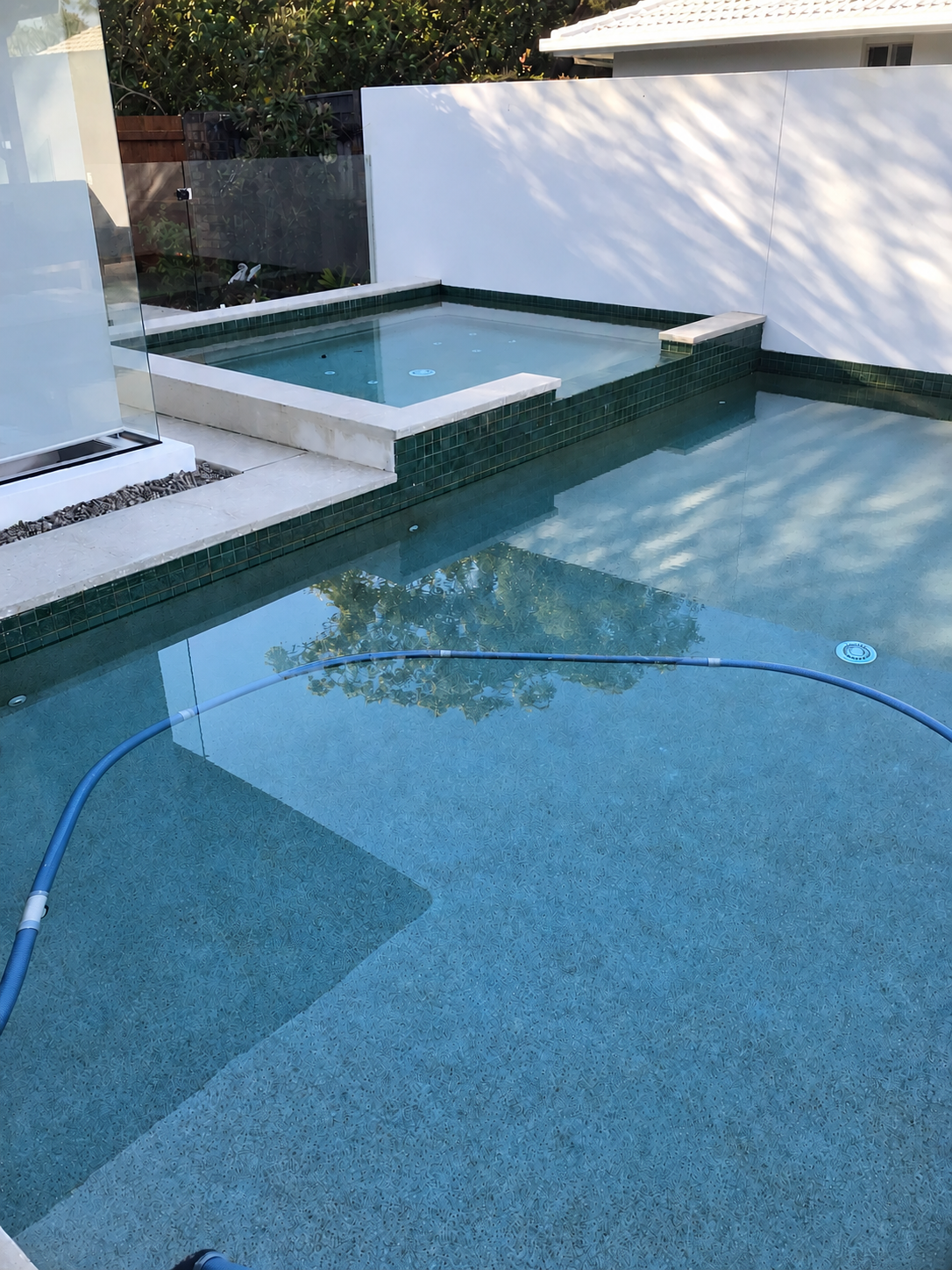 Swimming pool and raised spa with blue water, dark tiles and glass fencing in Mooloolaba