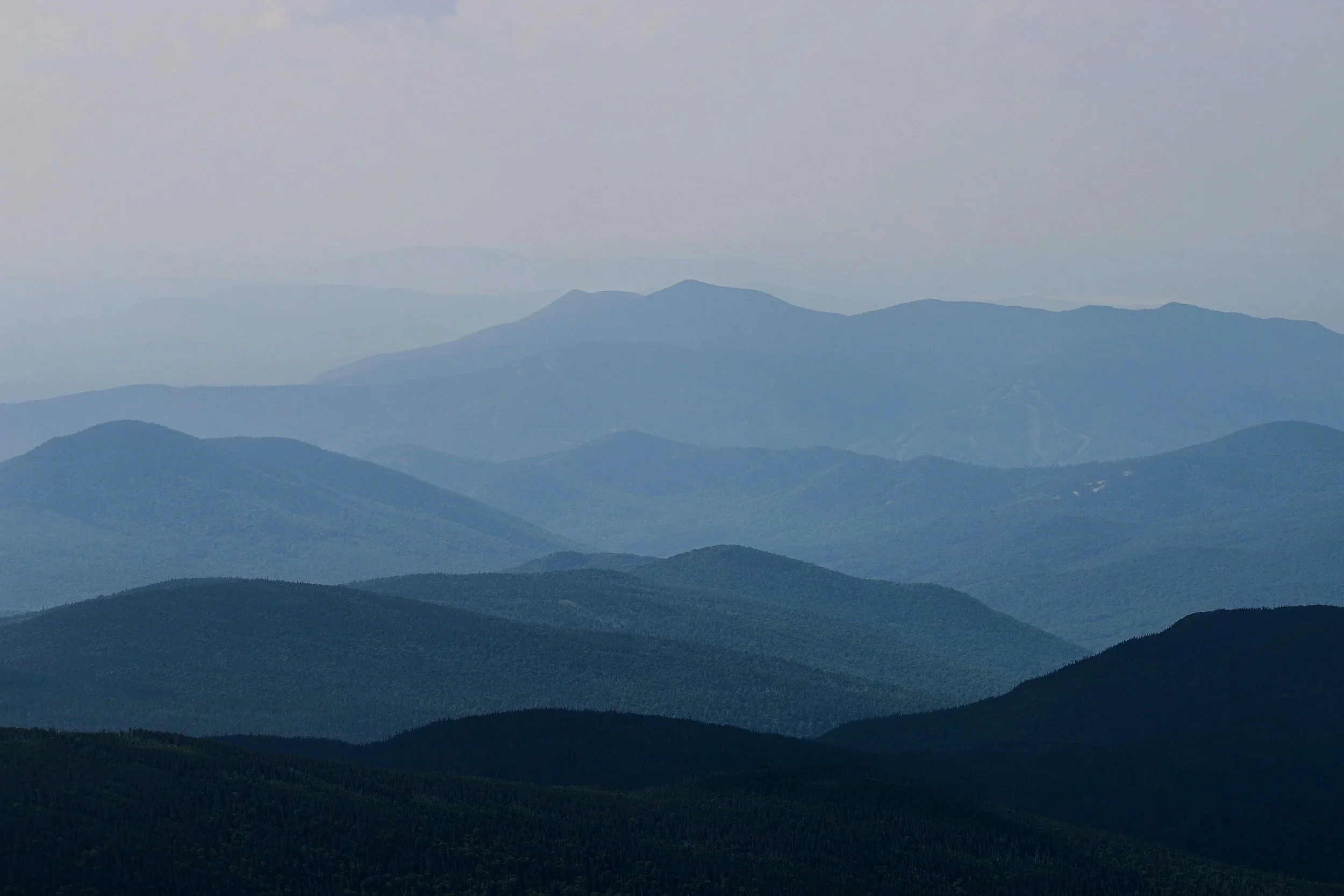 Layers of blue-green mountains under a light gray sky, with some mist or haze in the distance.