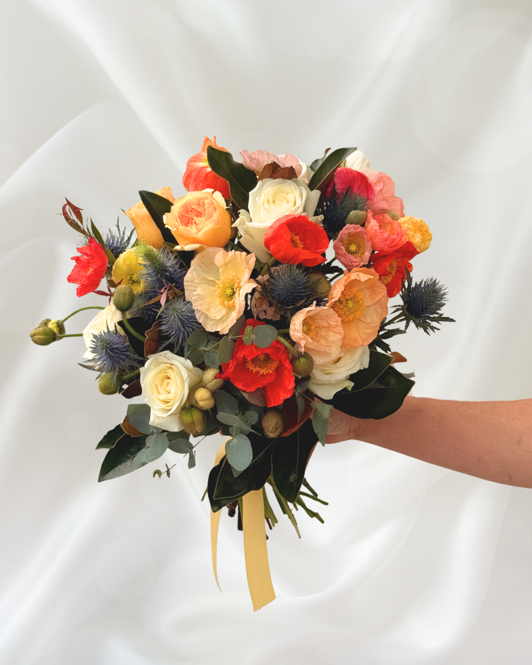 A person holding a colorful bouquet of flowers against a white fabric background.