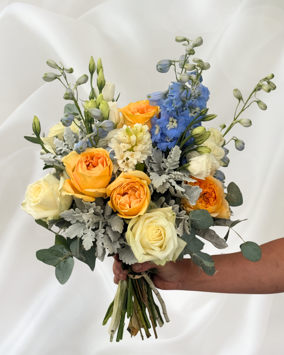 A person holding a colorful bouquet of flowers with white, yellow, orange, and blue blossoms against a white background.