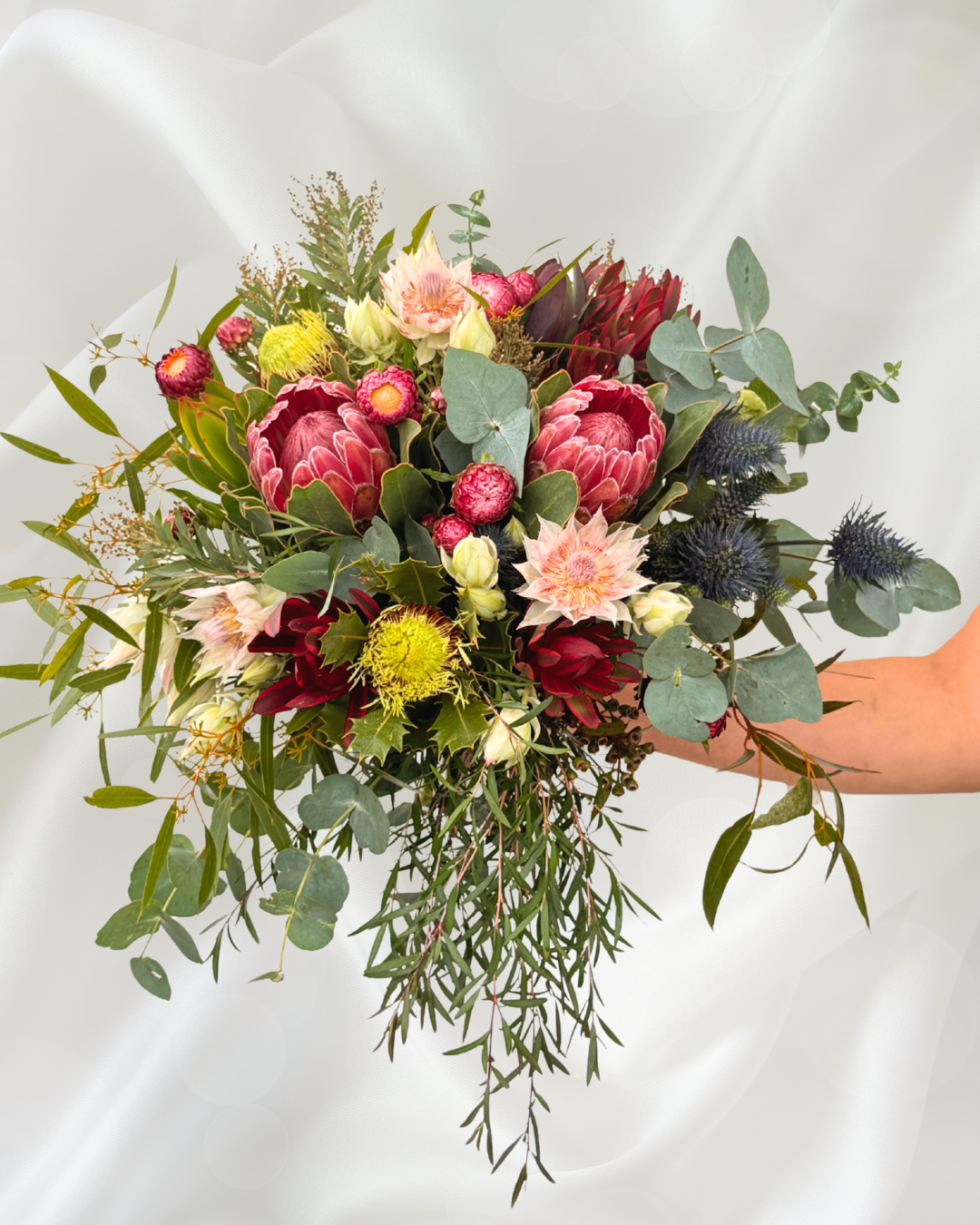 A person holding a bouquet of mixed flowers and greenery against a white background.