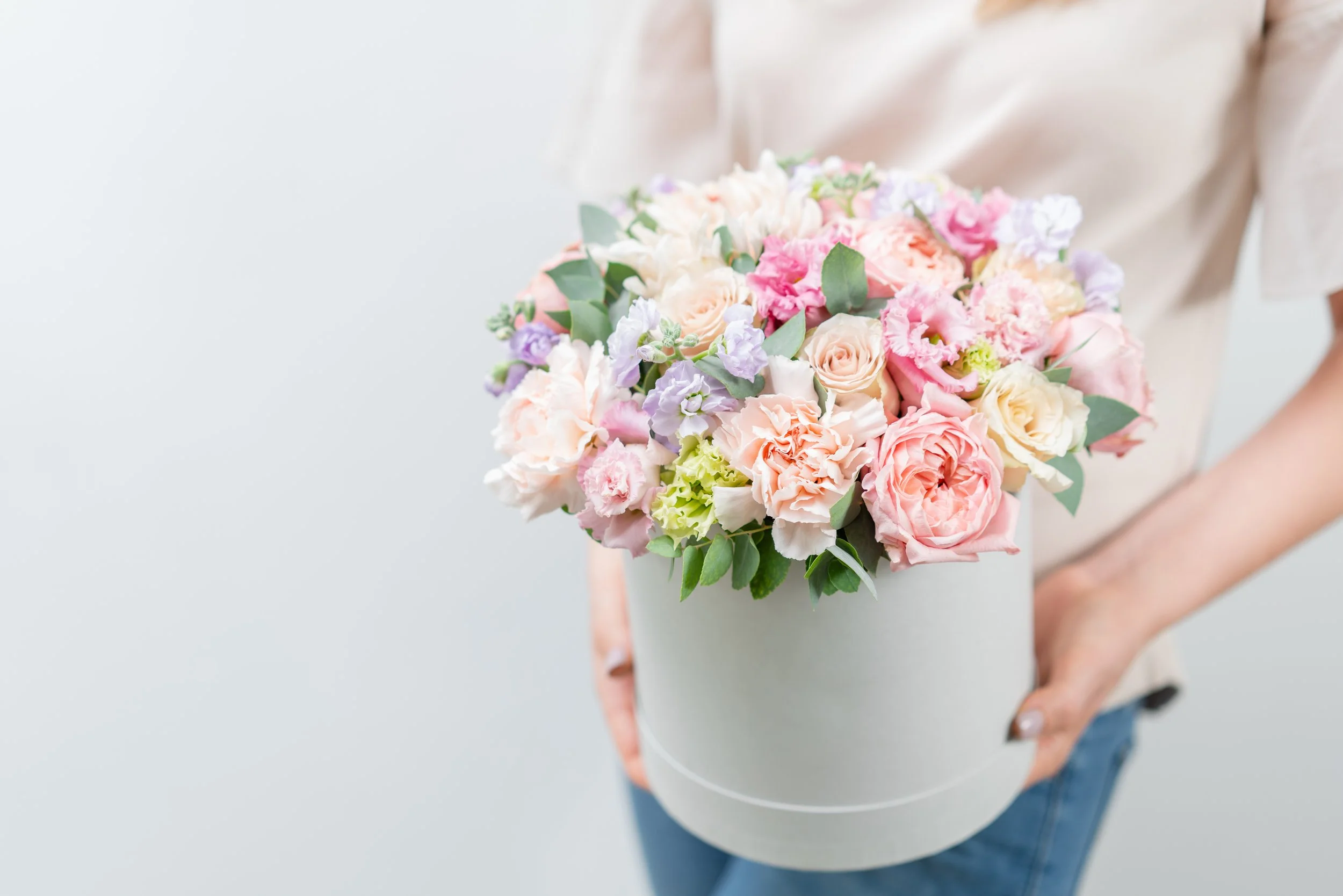 Person holding a white round box filled with light pink, peach, white, and purple flowers.