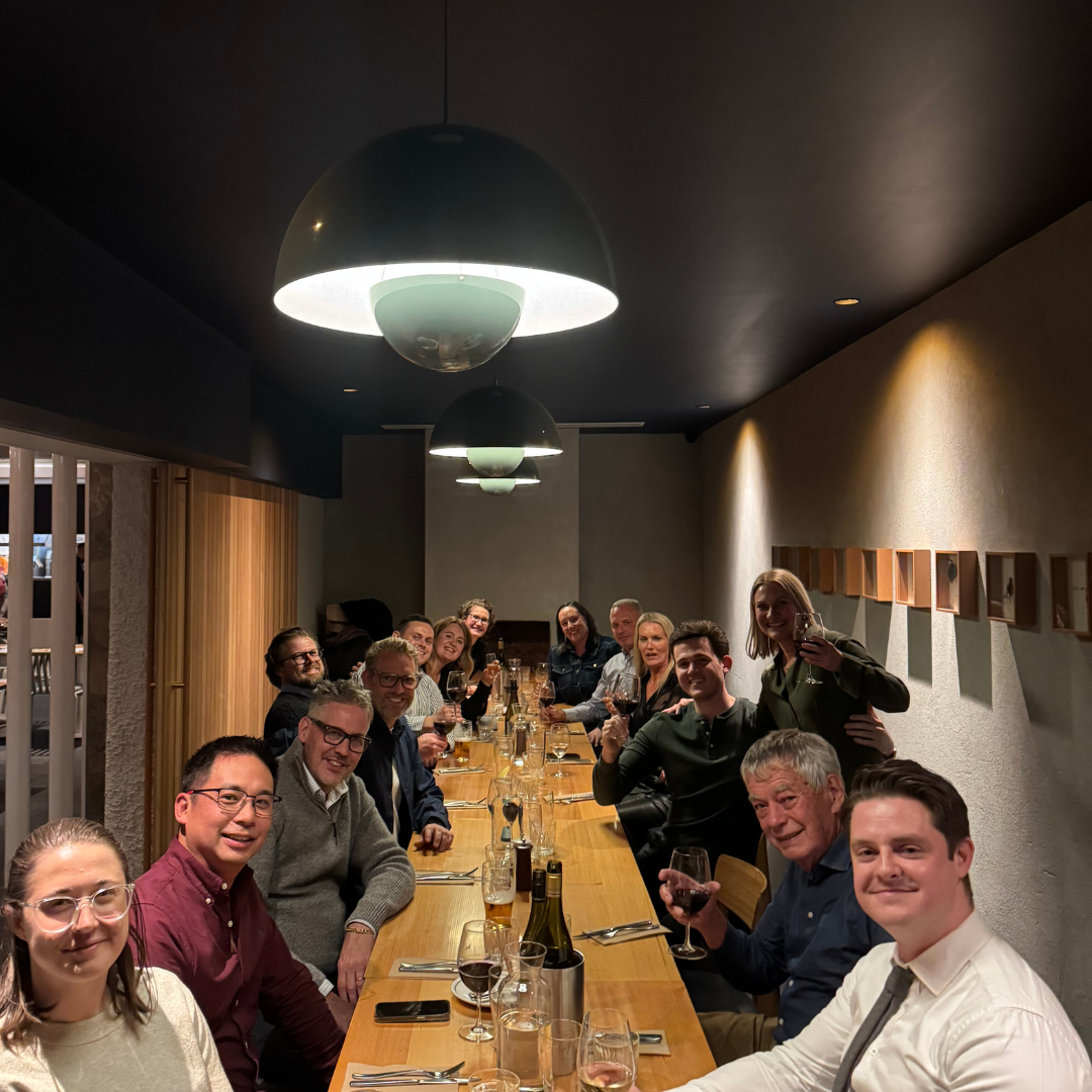 A group of people sitting around a long dining table enjoying a meal and drinks in a restaurant.