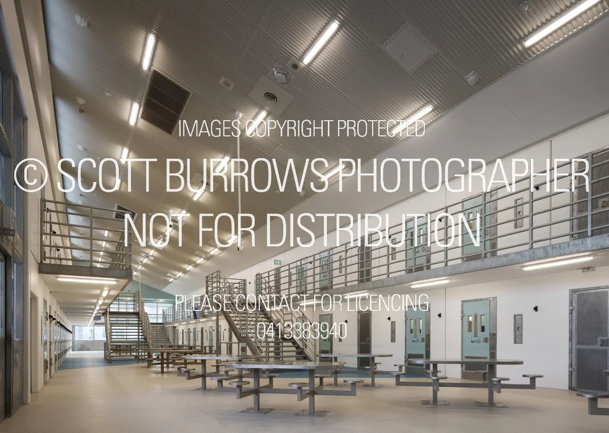 Interior of a modern correctional facility with multiple units, seating area, staircase, and metal lockers.
