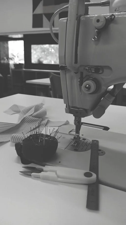 A sewing machine with various sewing tools and fabrics on a table in a well-lit room.