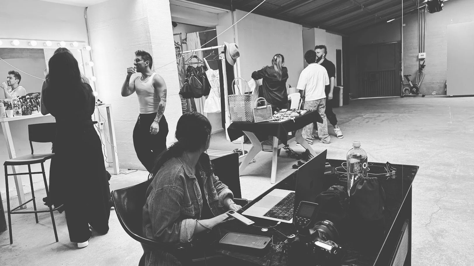 People preparing for a photo shoot or event in a studio with makeup, clothing, and photo equipment visible.
