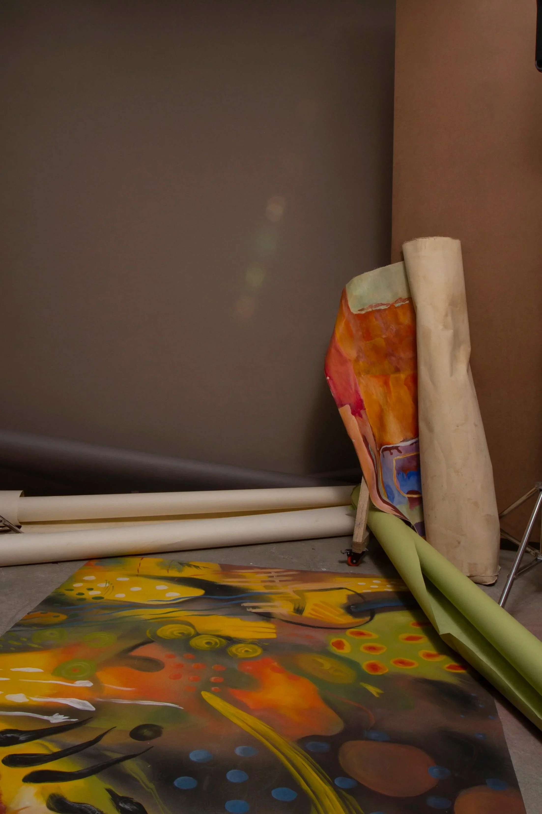 Colorful, abstract painting on the floor with rolled-up paper and paint tubes leaned against the wall.