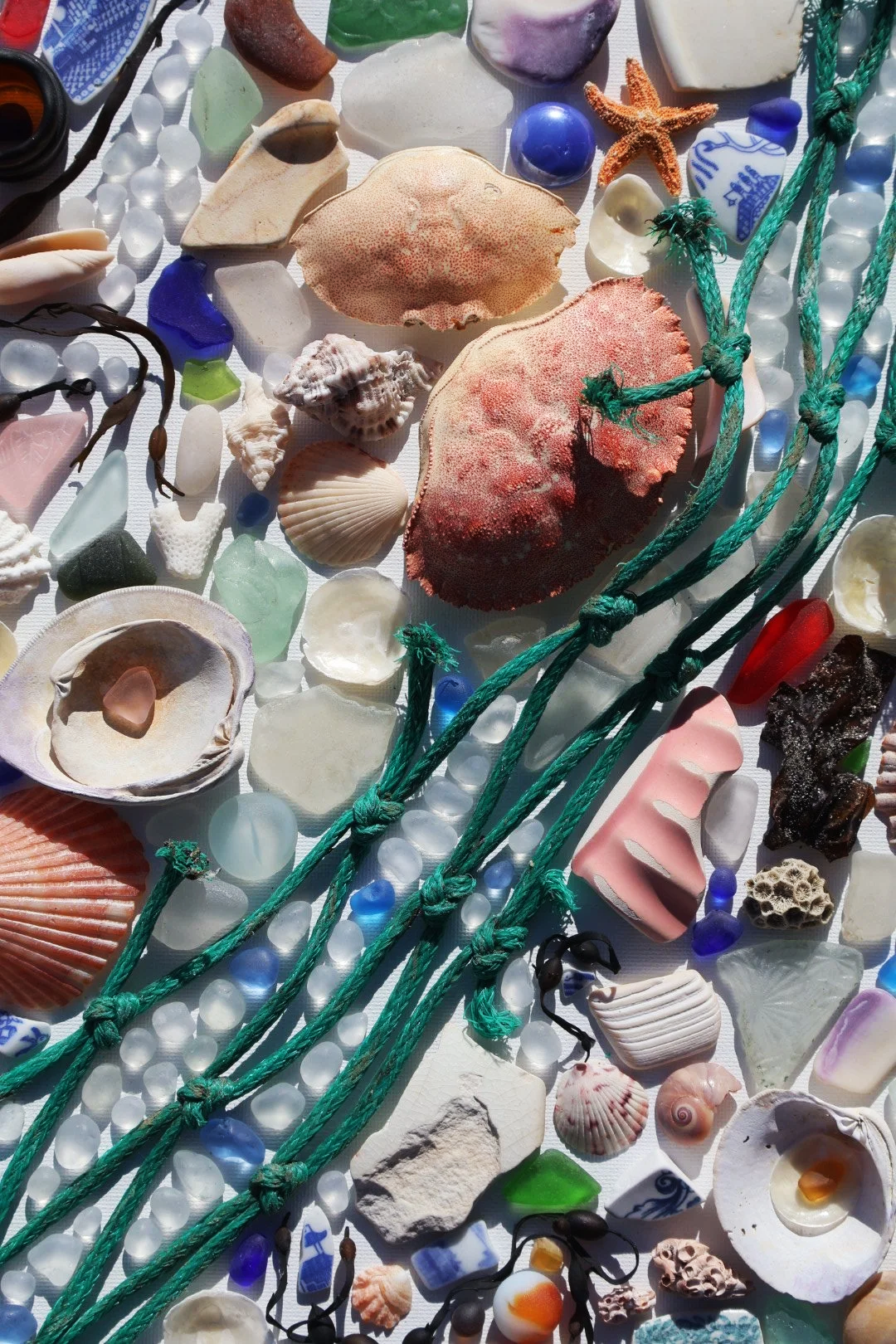 A collection of seashells, sea glass, and fishing nets on a surface, with various colors and shapes.