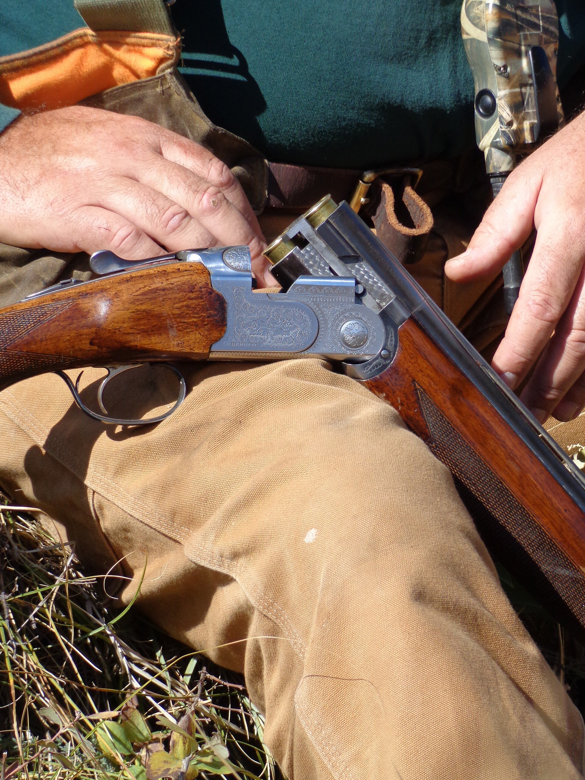 A hunter's hands on a broken-open over-under shotgun during a break on a bird hunt.