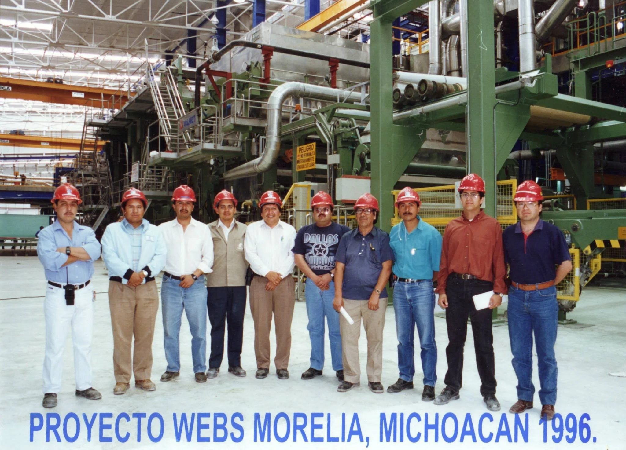 Grupo de personas con cascos de seguridad en una planta industrial, posando para una foto. Texto en la parte inferior que dice: "Proyecto Webs Morelia, Michoacán 1996".
