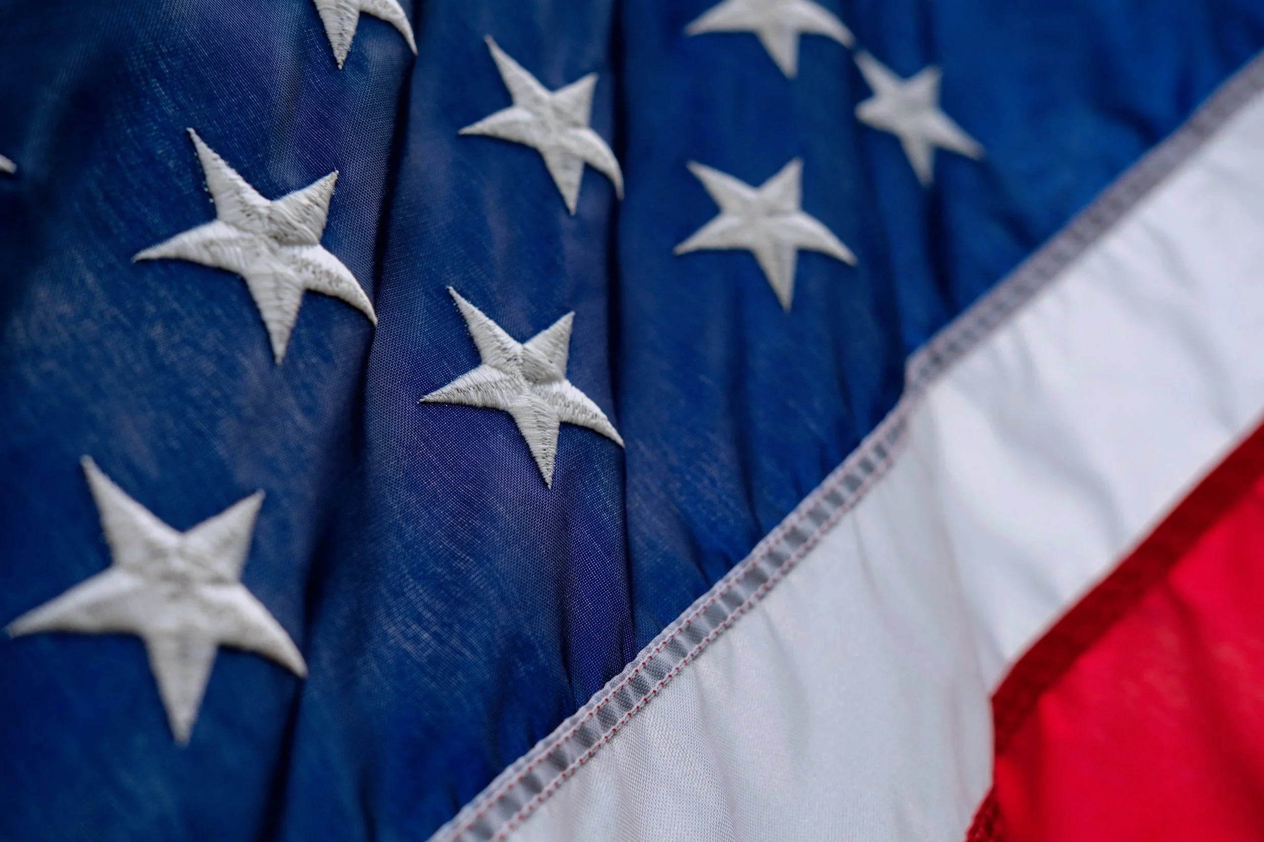 Close-up of a fabric American flag with white embroidered stars on and sewn red and white stripes.