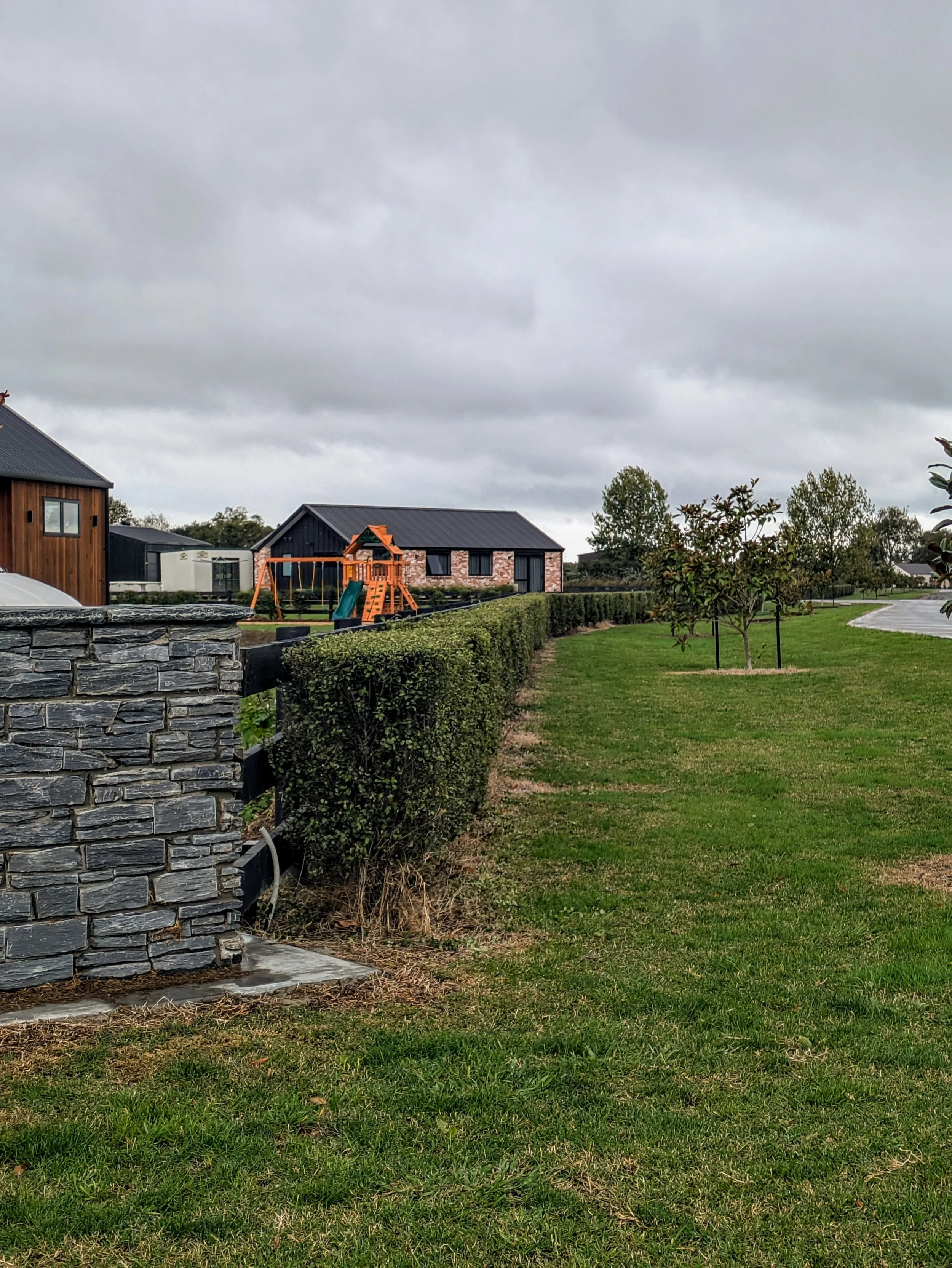 Landscaped backyard with lawn, stone retaining wall, trimmed hedges and young trees on a Waikato property
