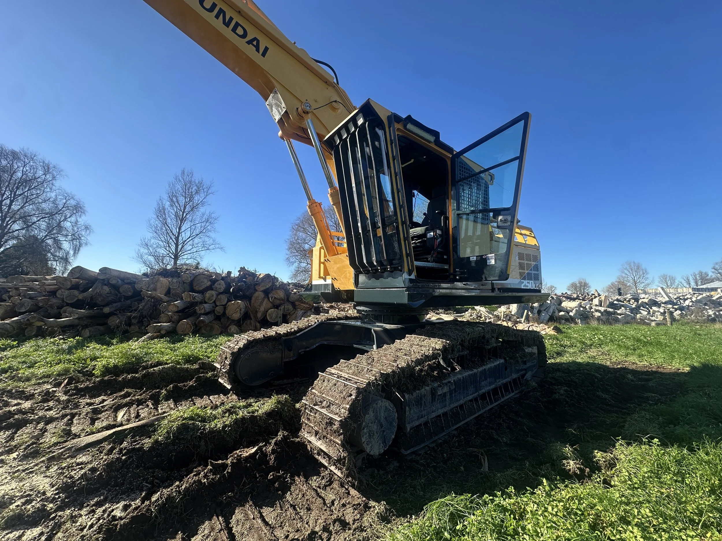 Yellow excavator clearing logs and debris on a rural Waikato site