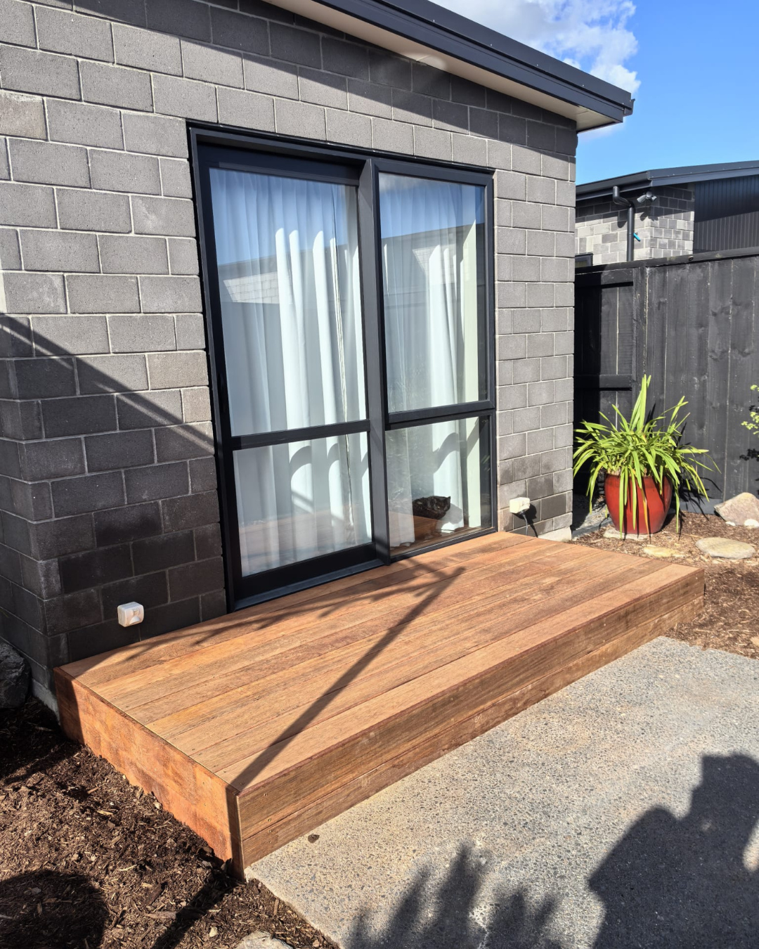 Timber deck installed outside a brick home with sliding door and potted plant
