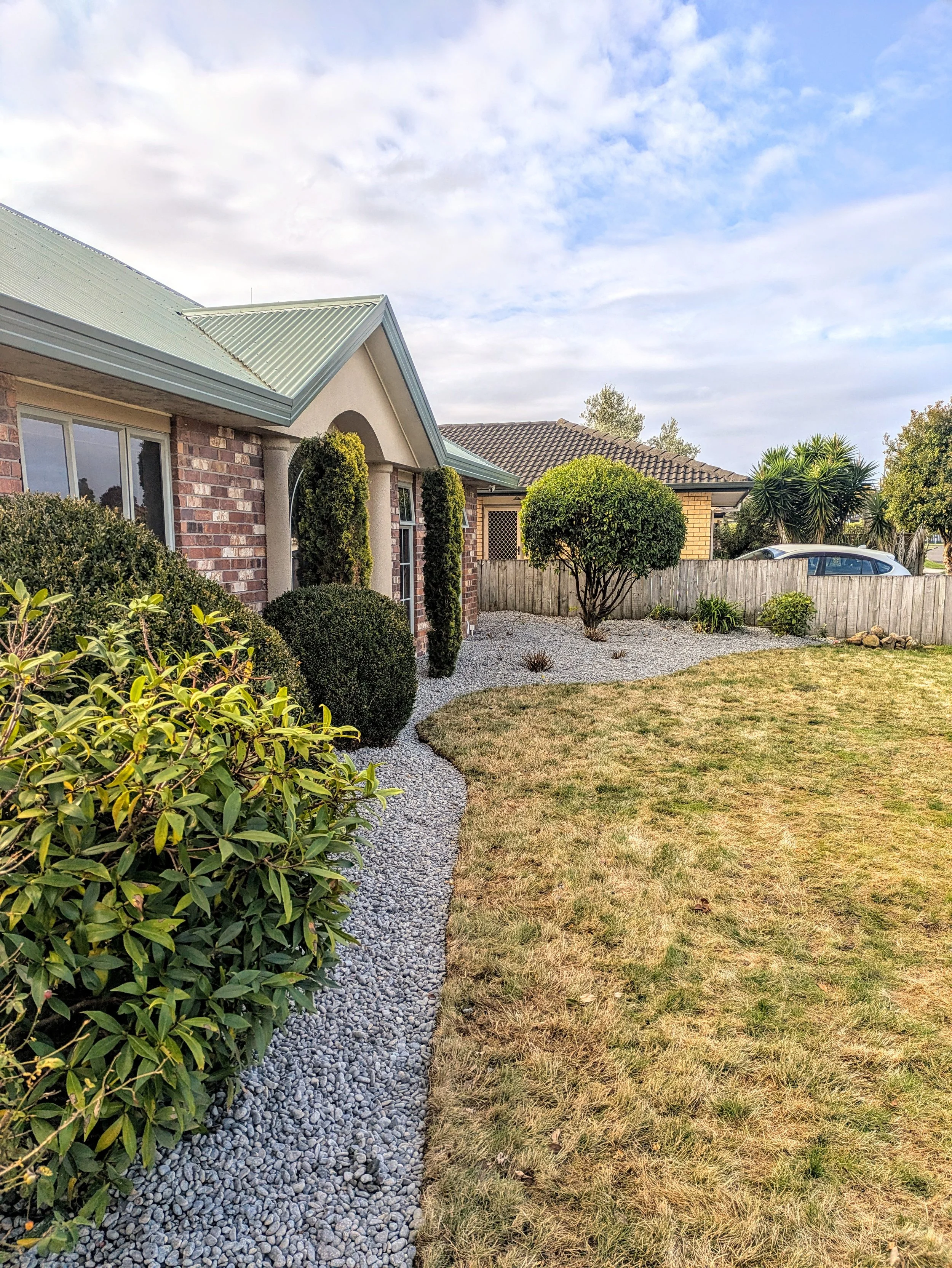 Landscaped residential front yard with gravel path, trimmed gardens and lawn in Waikato