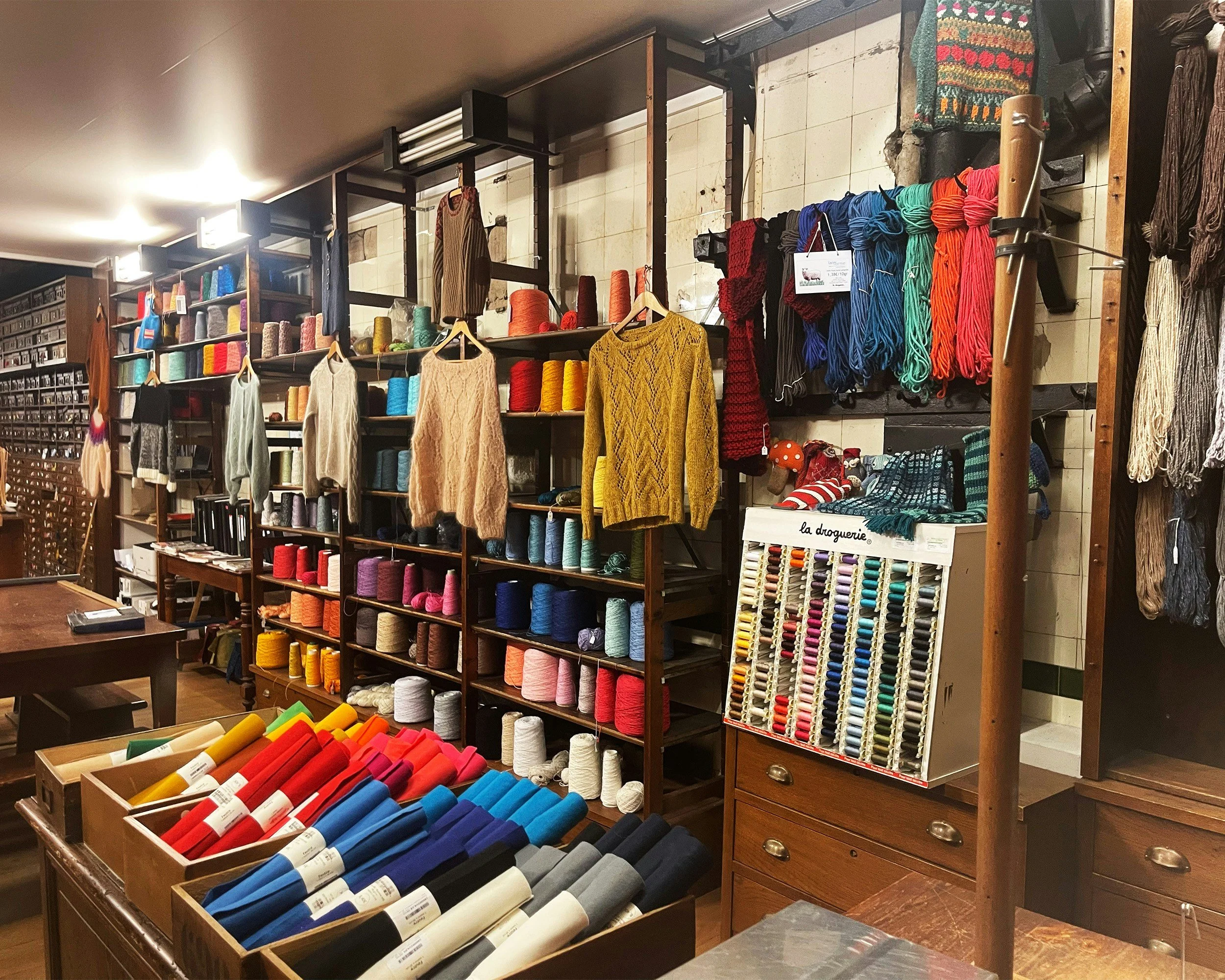Store interior with shelves of colorful yarn, knitted sweaters, and sewing supplies.