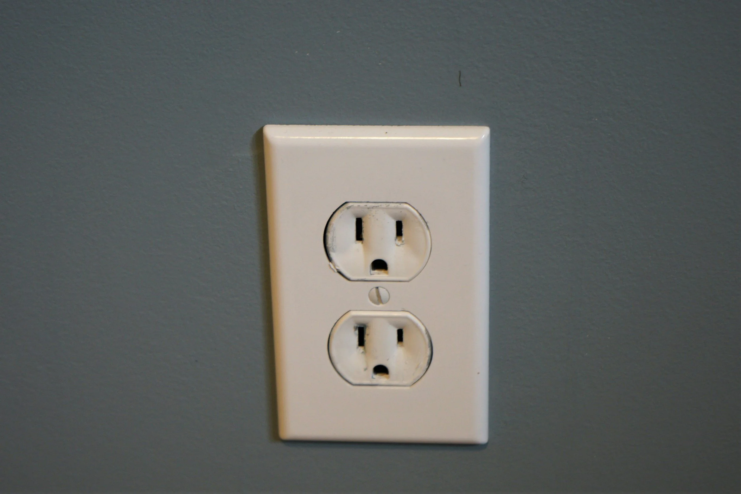 White electrical outlet with two power sockets mounted on a gray wall.