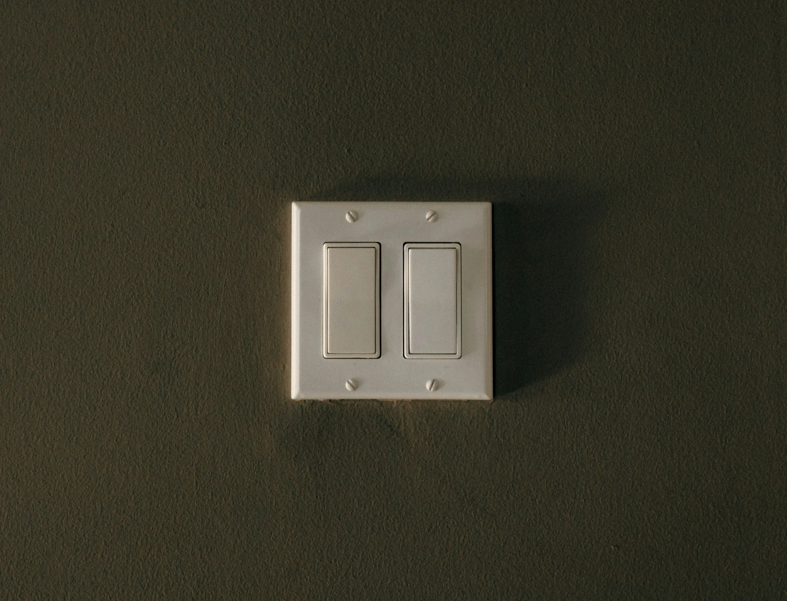 A white double light switch mounted on a textured gray wall.