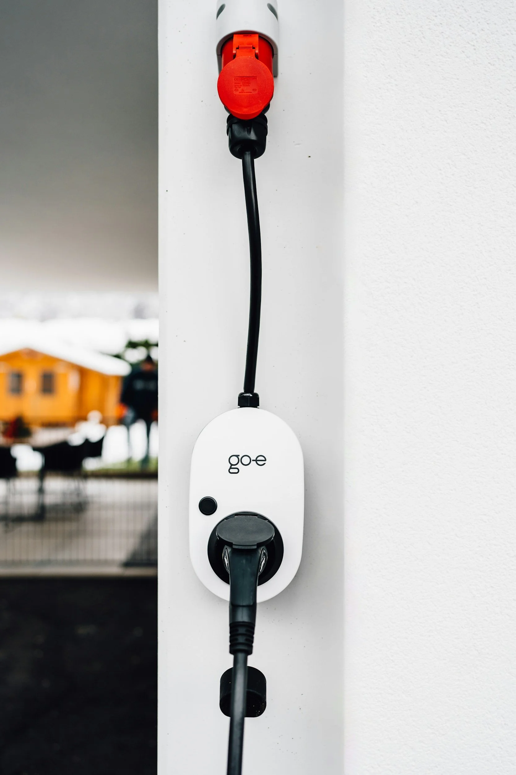 Electric vehicle charging station with a white charger labeled 'goe' mounted on a white wall, with a black charging cable plugged in.