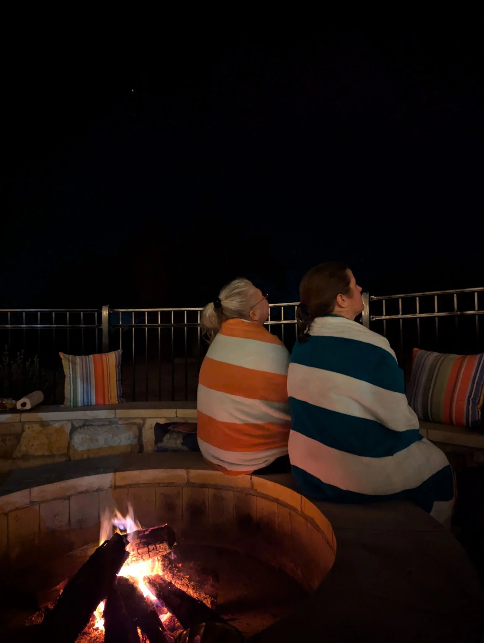 Guests wrapped in blankets enjoying an evening by the fire pit under the night sky.