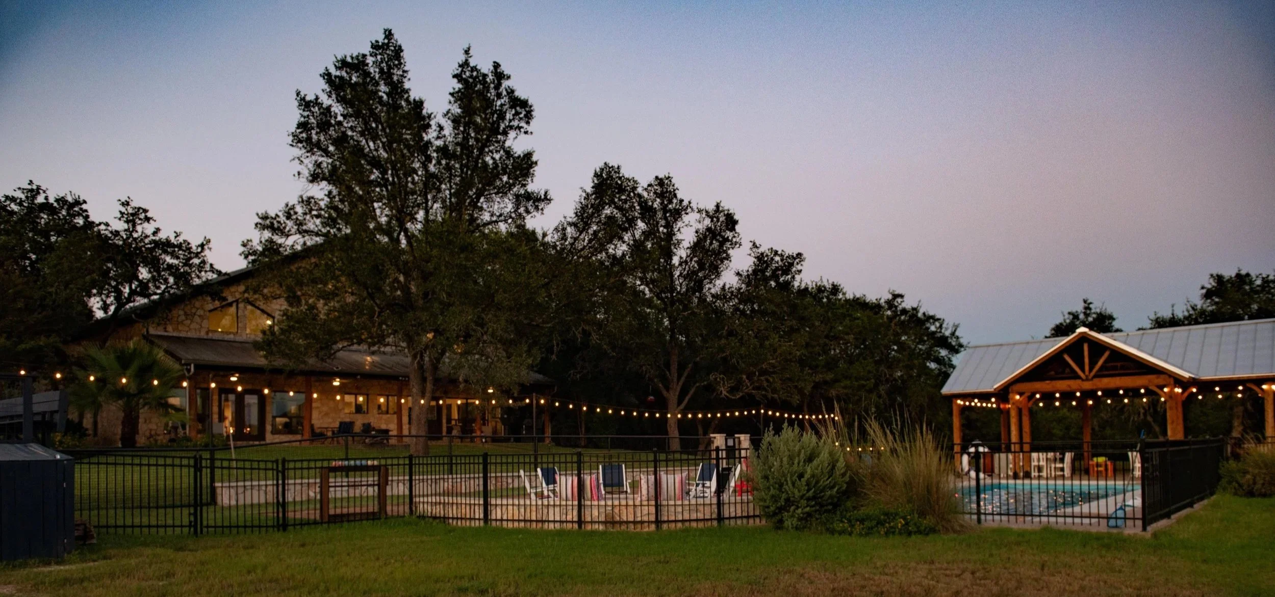 Main House, pool and covered pavilion illuminated at dusk at The Gathering in Wimberley, Texas.