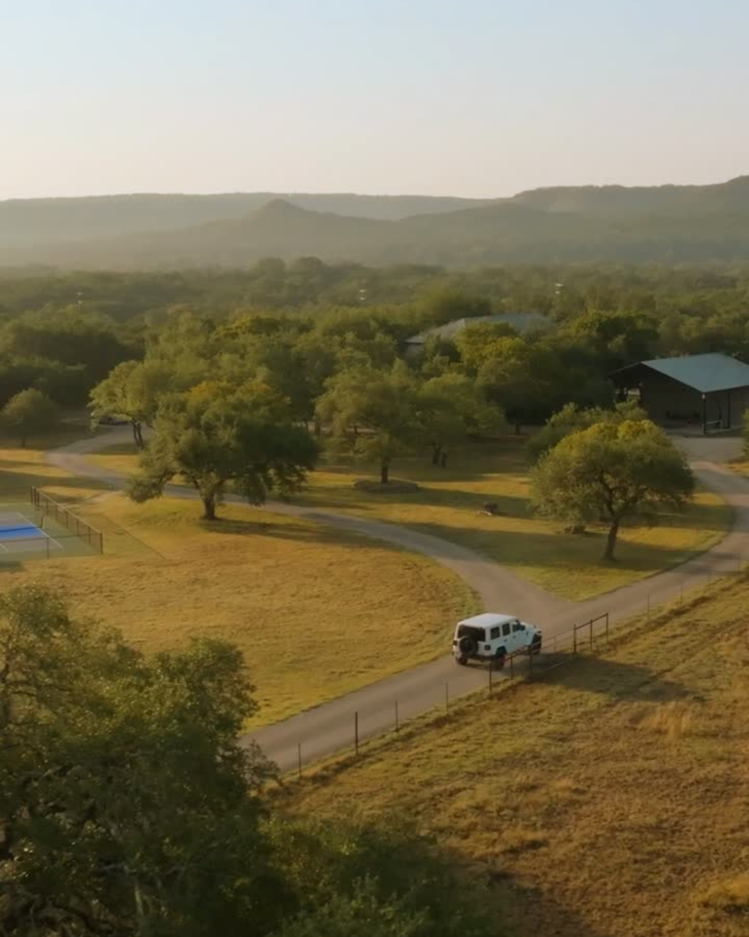 Aerial view of The Gathering’s private acreage, oak trees, pickleball court, and surrounding Texas Hill Country near Wimberley, Texas.