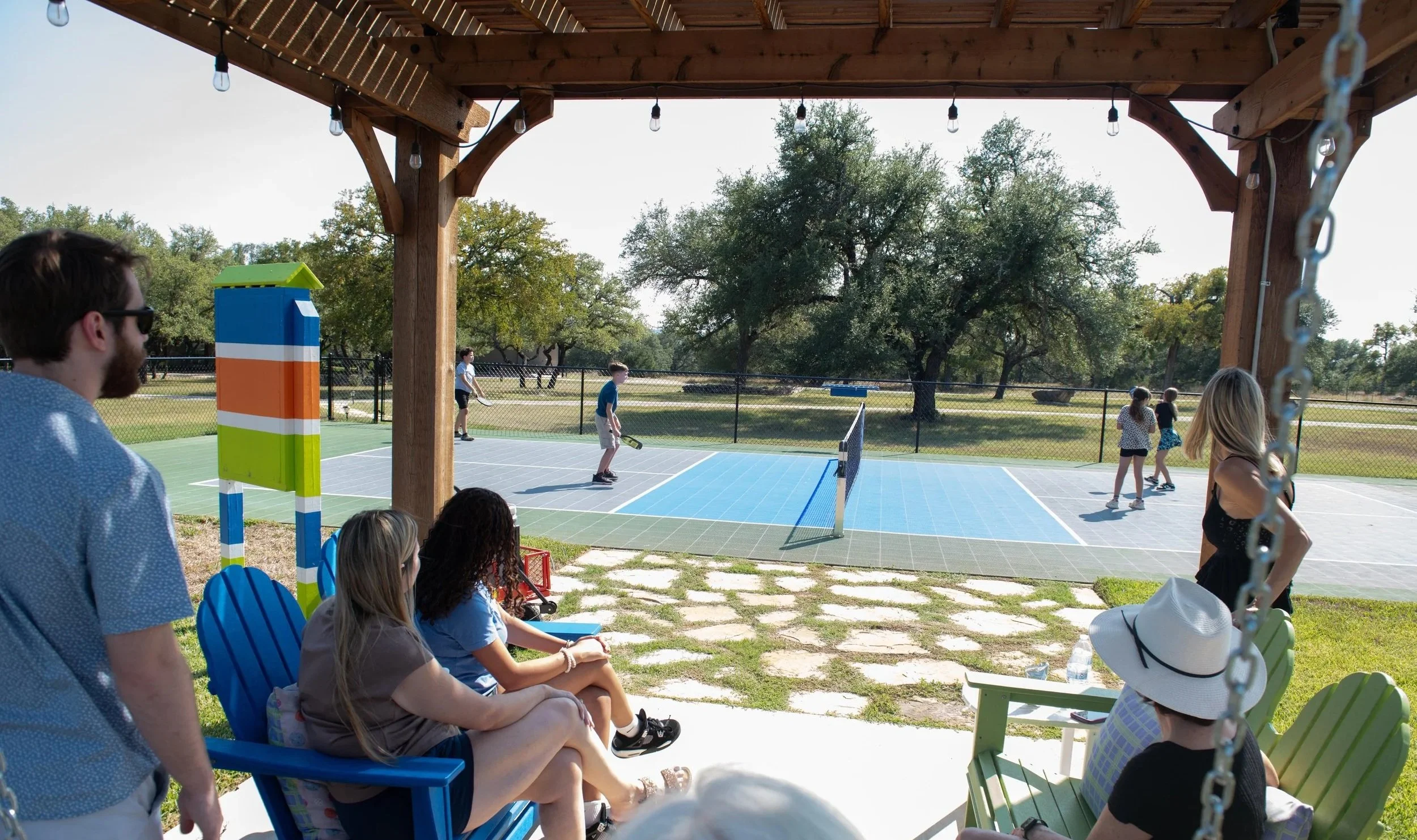 Guests playing pickleball while others watch from shaded seating beside the court at The Gathering in Wimberley, Texas.