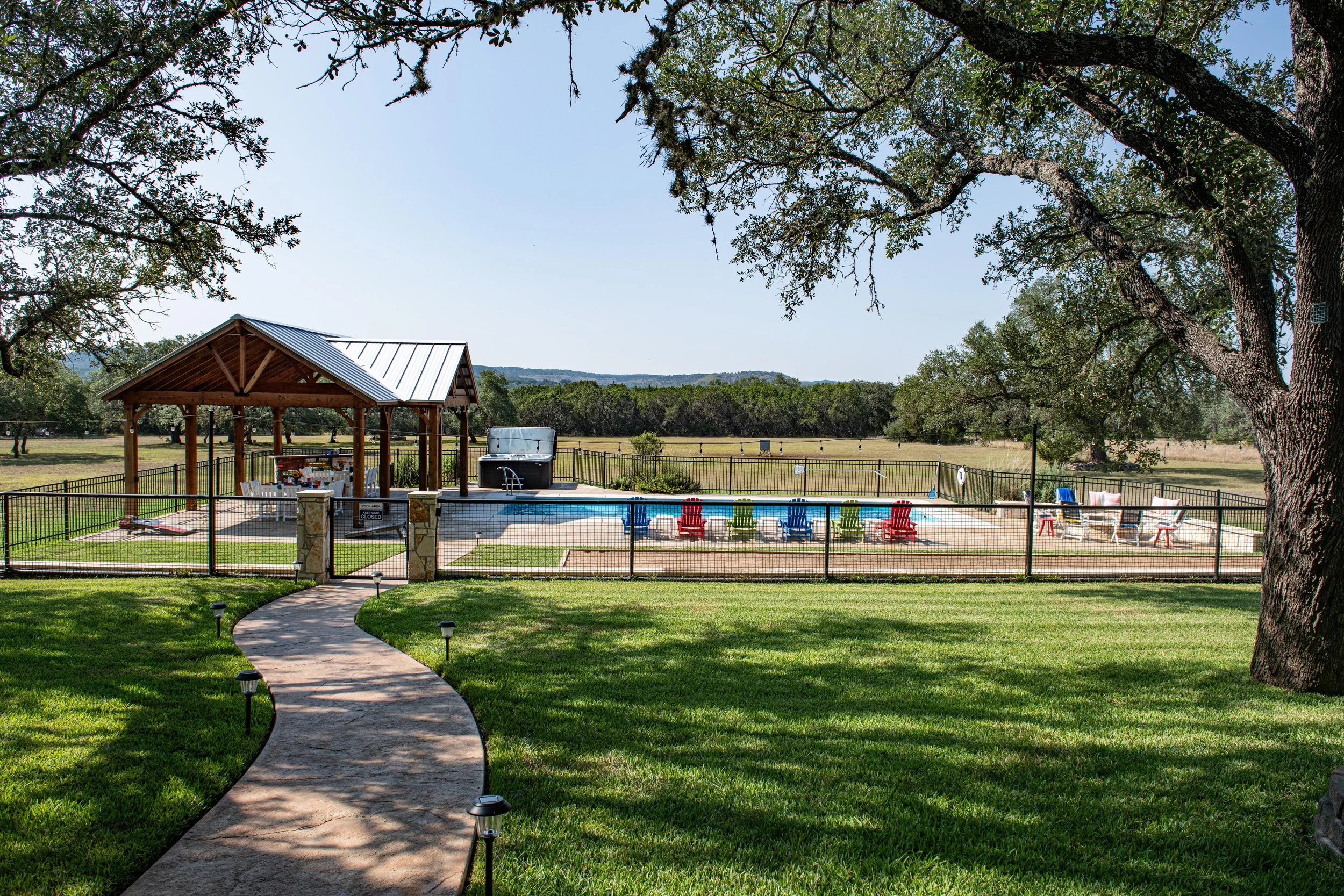 View of back yard leading to fenced pool, hot tub, firepit area and Hill Country views beyond.
