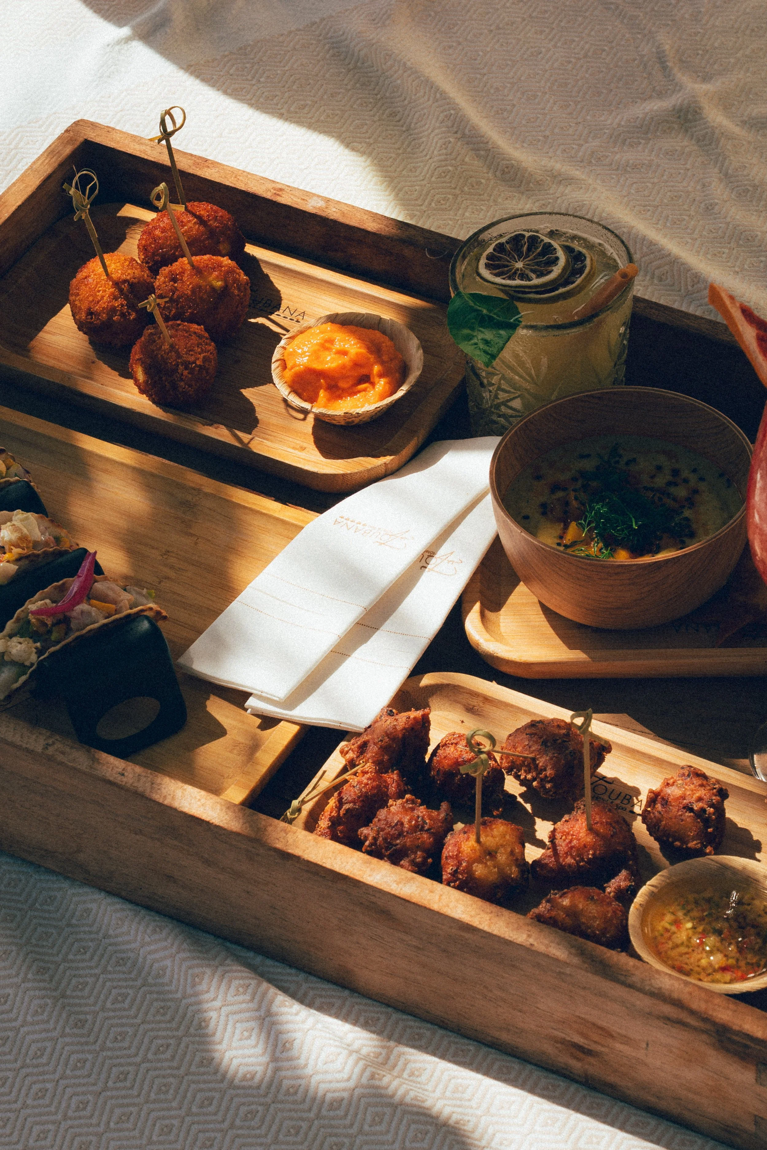 Plateau en bois avec des boulettes frites, une sauce orangée, une boisson citronnée avec des rondelles de citron et une feuille, un bol de soupe, et des petits morceaux de poulet frit.