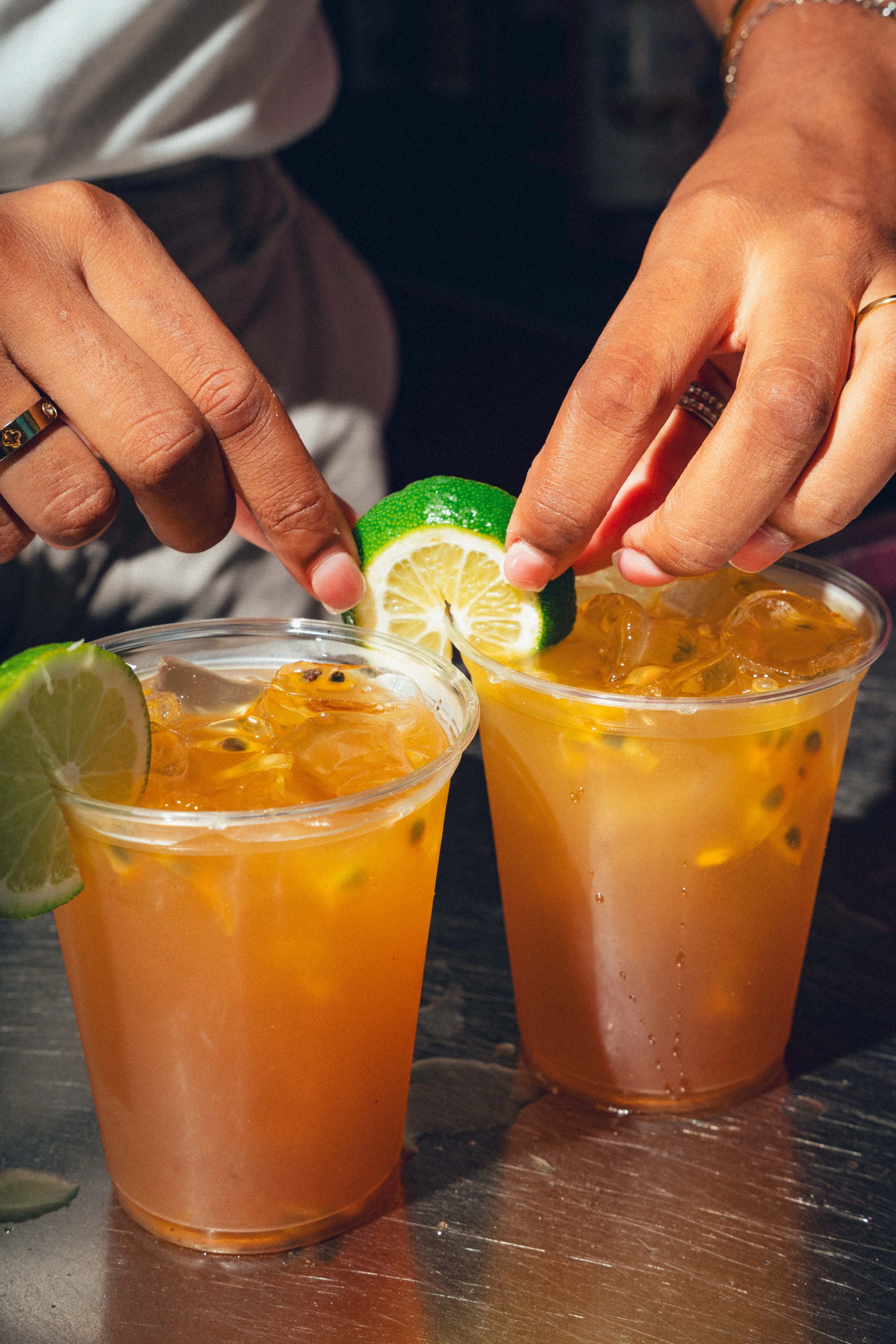 Deux verres de boisson orange œil de perdrix avec des tranches de citron vert en garniture, sur une table en bois, avec une personne utilisant une tranche de citron pour garnir la boisson.