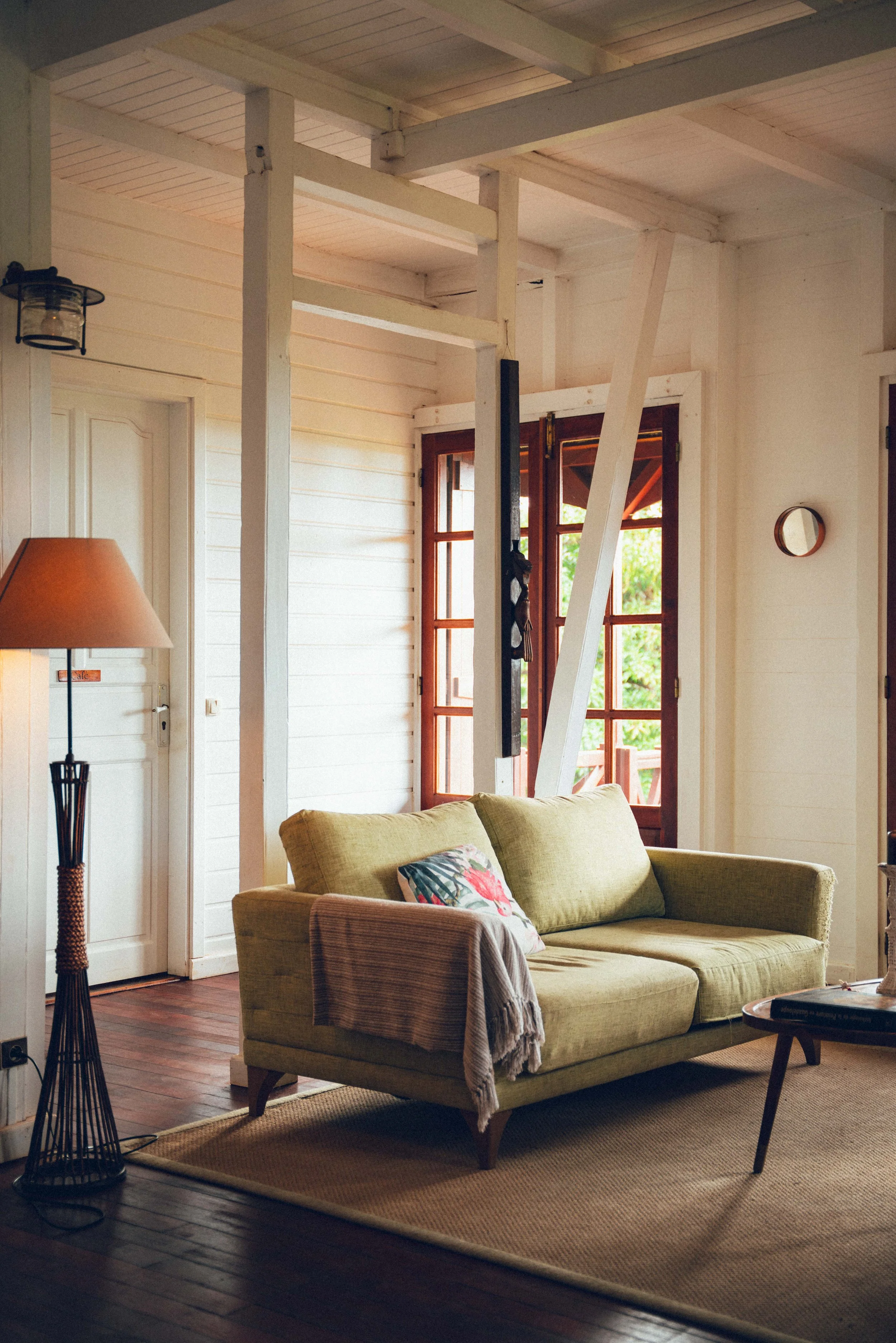 Salon intérieur avec un canapé vert, une table ronde en bois, un tapis et une grande fenêtre laissant entrer la lumière naturelle.