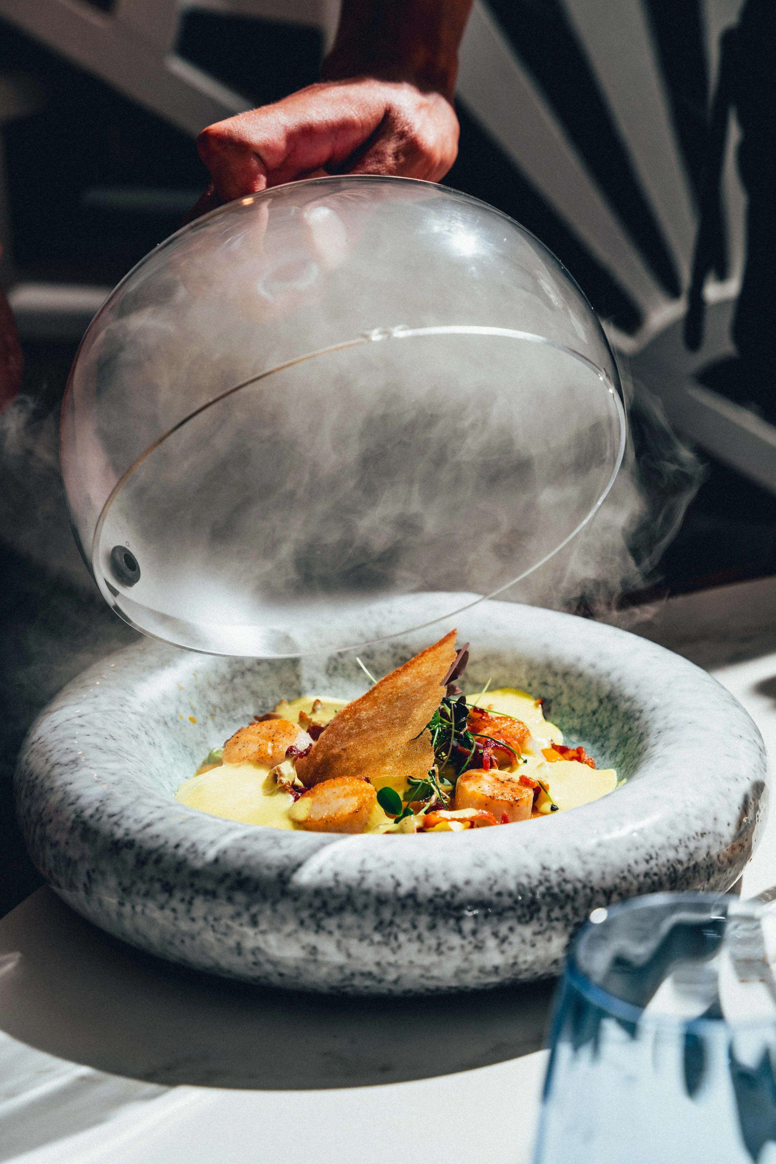 Photographie culinaire d'un plat gastronomique élégant dans un bol de pierre, contenant des morceaux de poulet, des herbes, une sauce ou purée, avec un éclairage naturel.